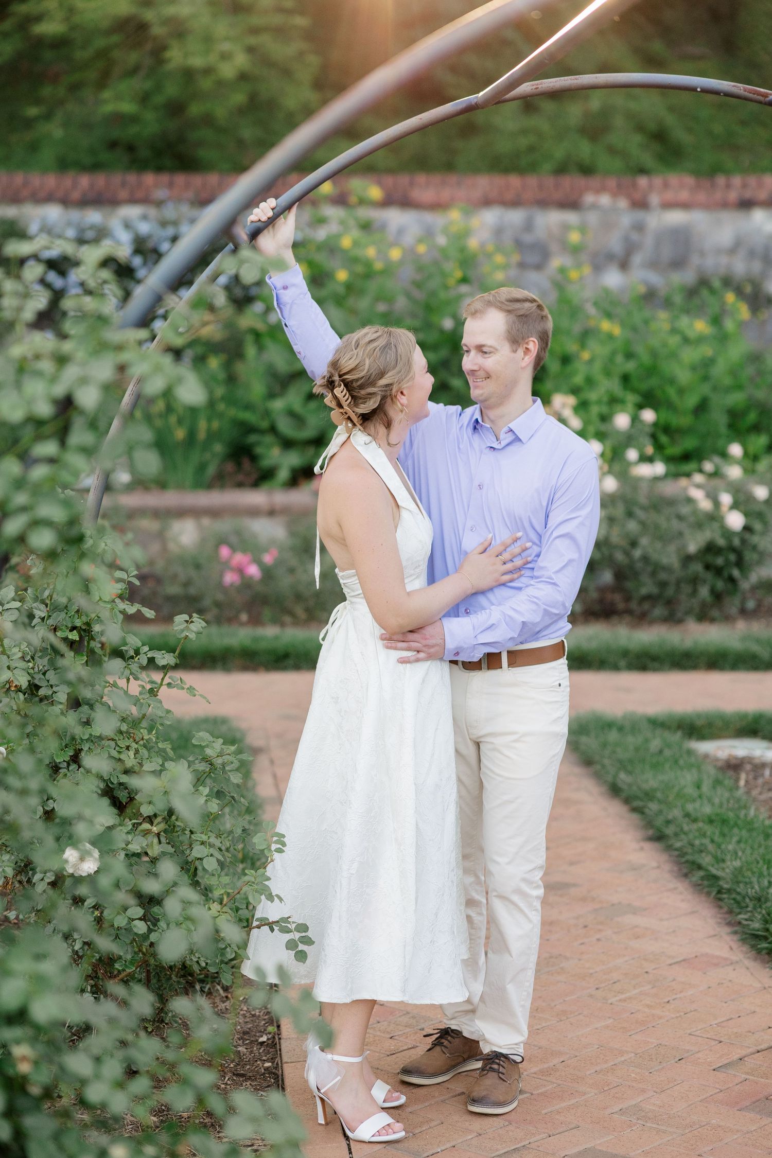 A couple dances together on a brick path surrounded by a lush garden setting.
