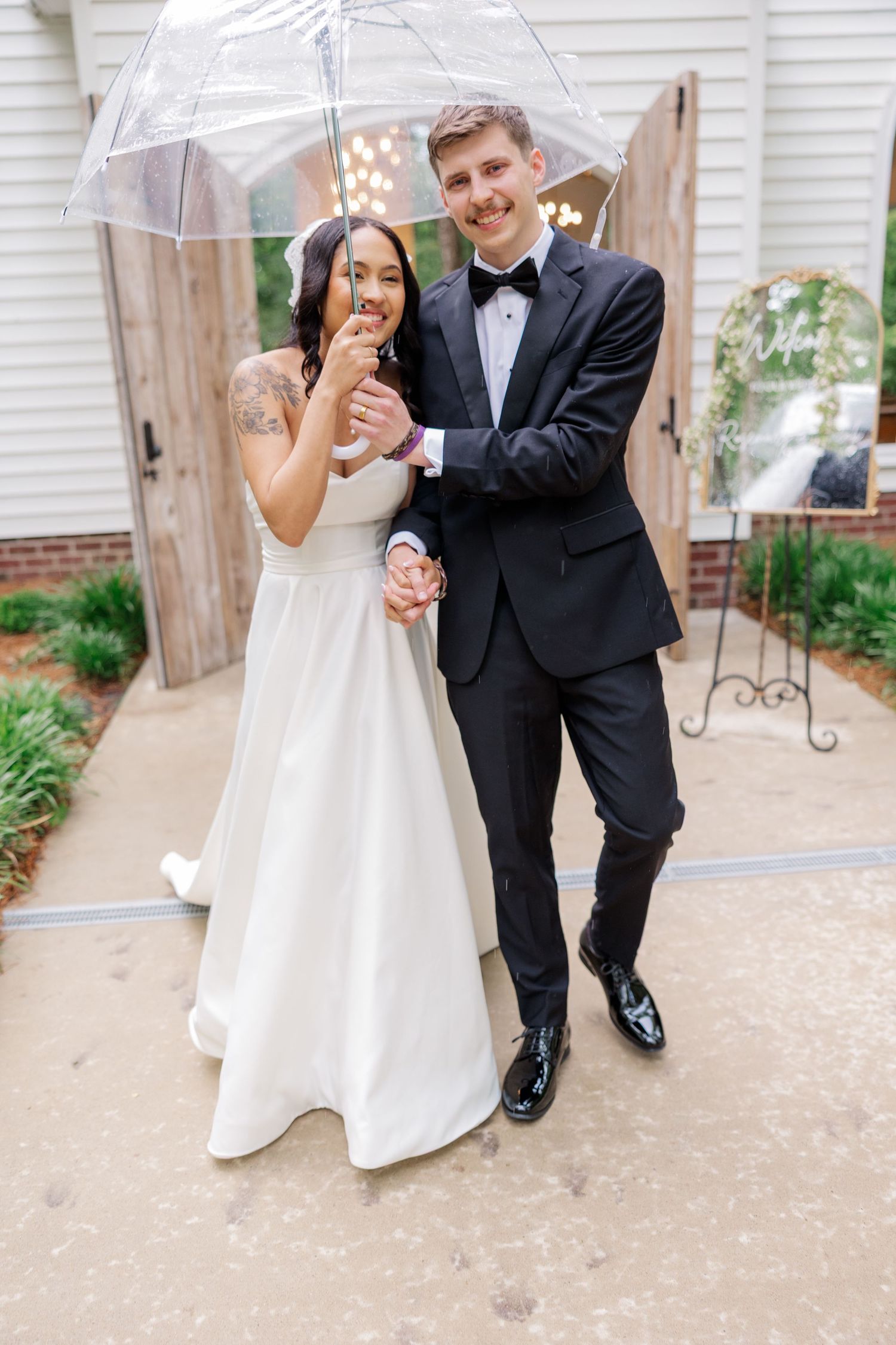 Newlyweds holding umbrellas while dancing and laughing in the rain on their wedding day.