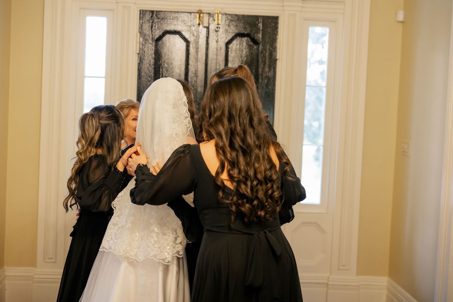 Final bridal preparations with attendants in dark dresses in a beautifully decorated room.