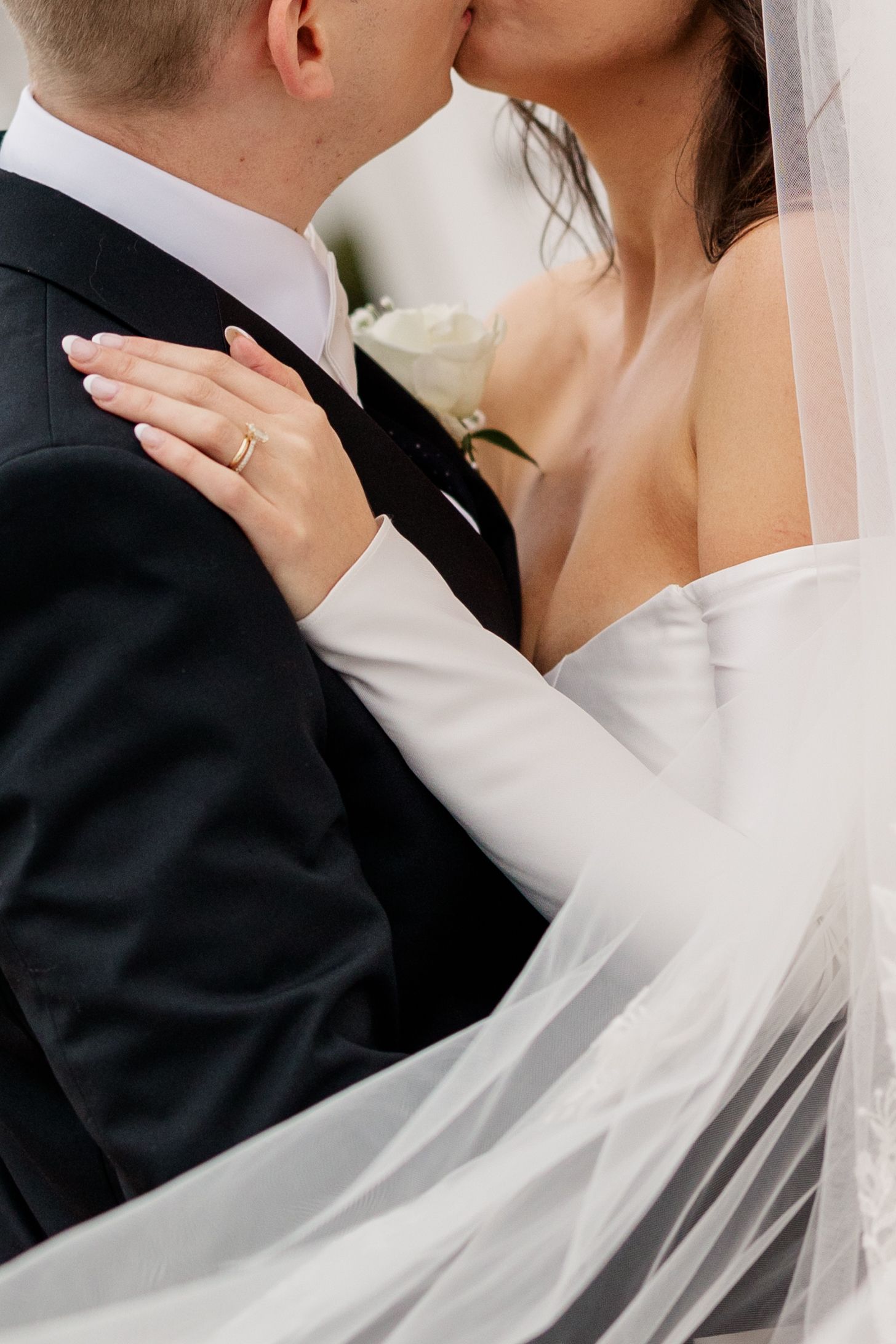 A close-up of newlyweds sharing an intimate moment with veil and wedding ring visible.