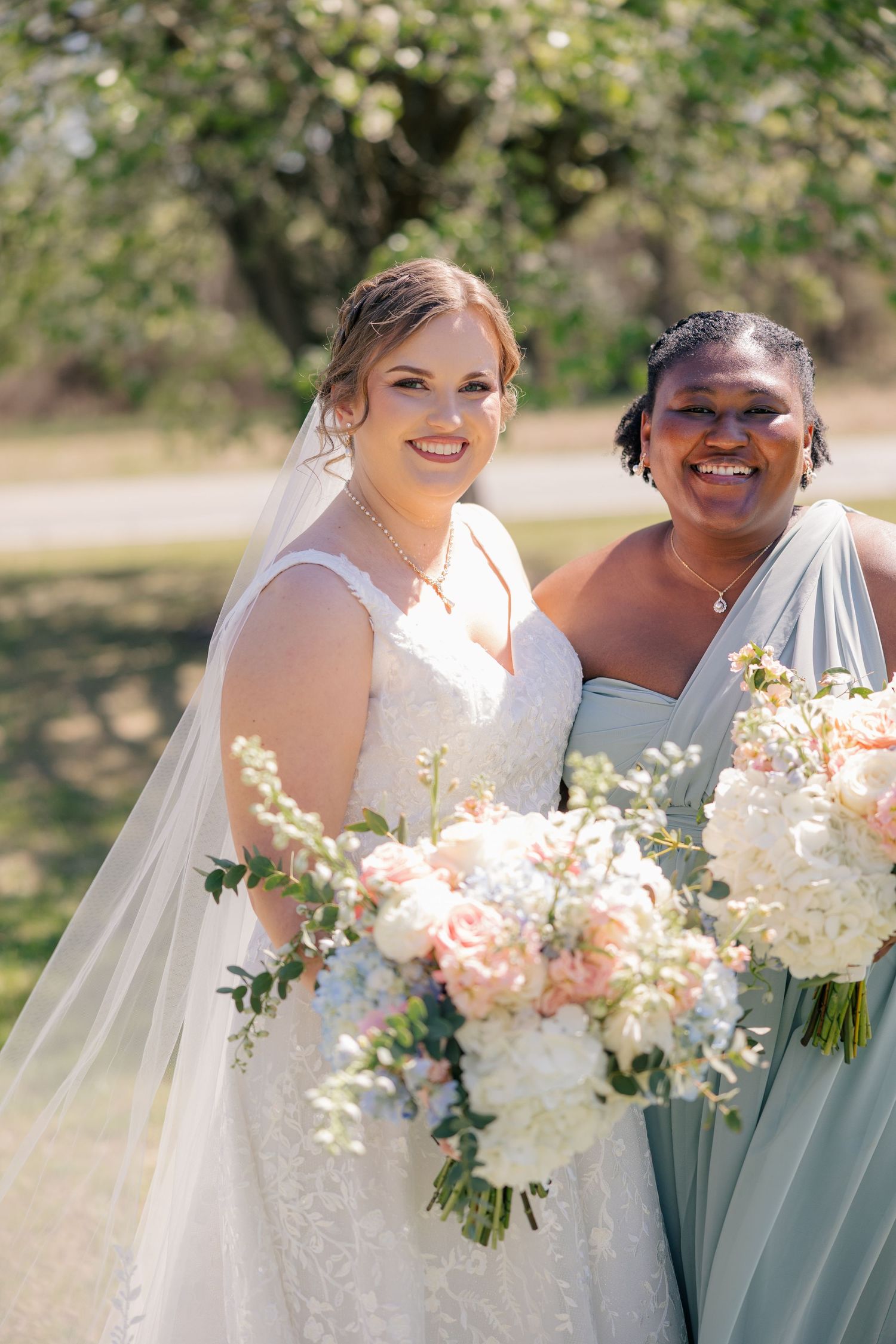 Wedding party holding beautiful blush and ivory floral bouquets in a sunny outdoor setting.