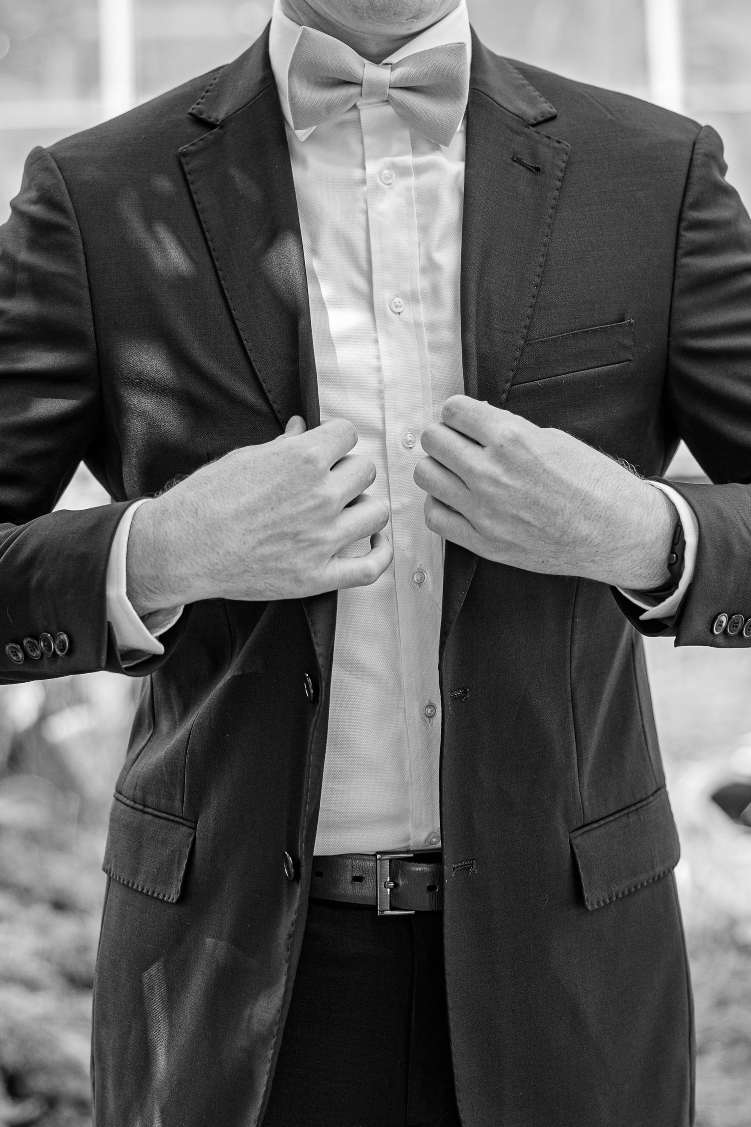 Close-up of groom adjusting black tuxedo jacket and bow tie.