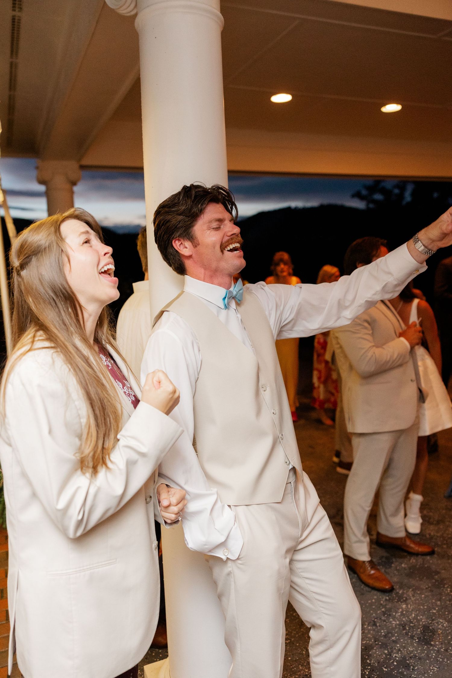 Wedding guests in white attire dancing energetically at an evening reception.