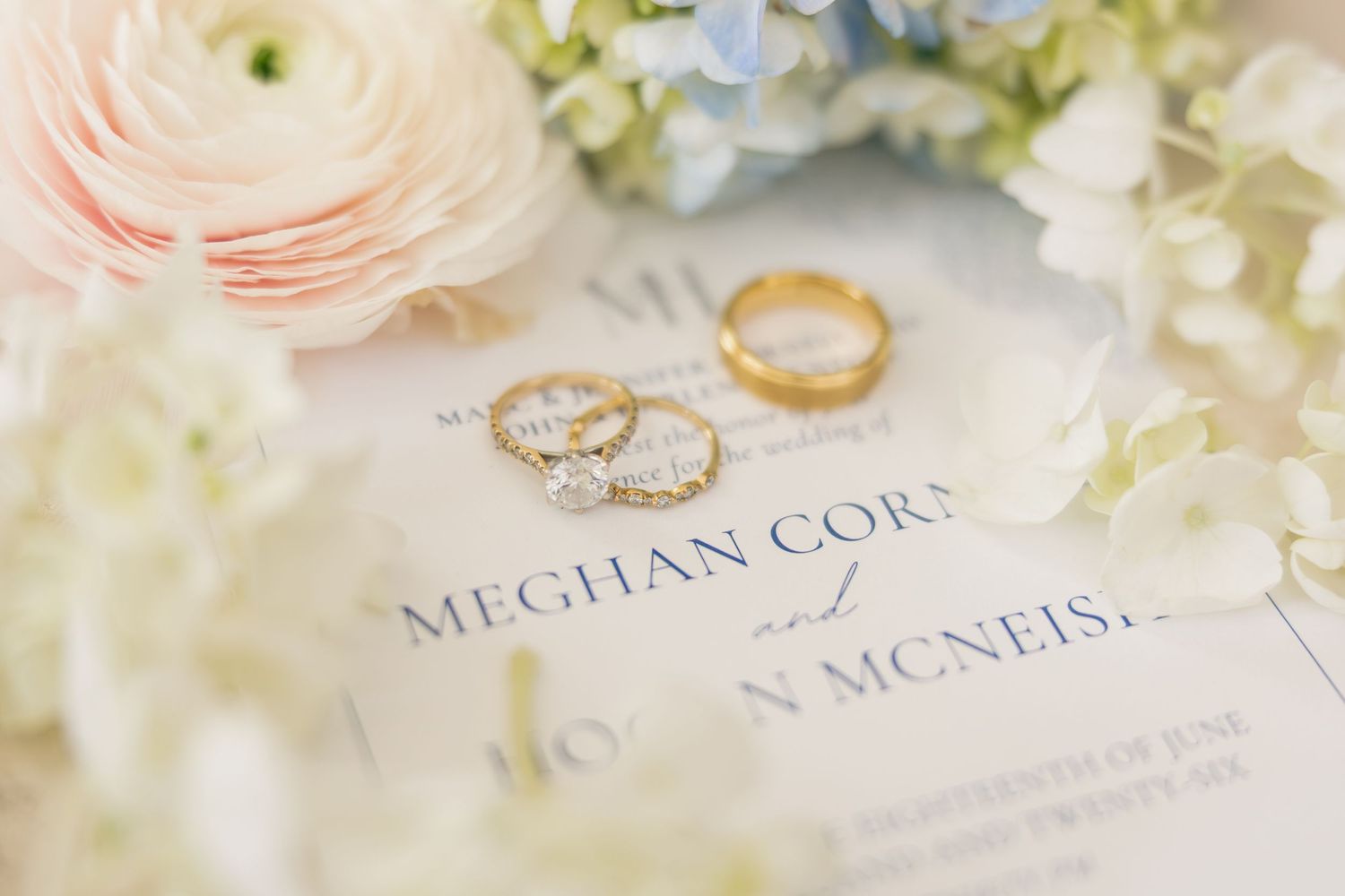 Gold wedding rings rest on elegant wedding invitations for Meghan Corn and Morgan McNeish.