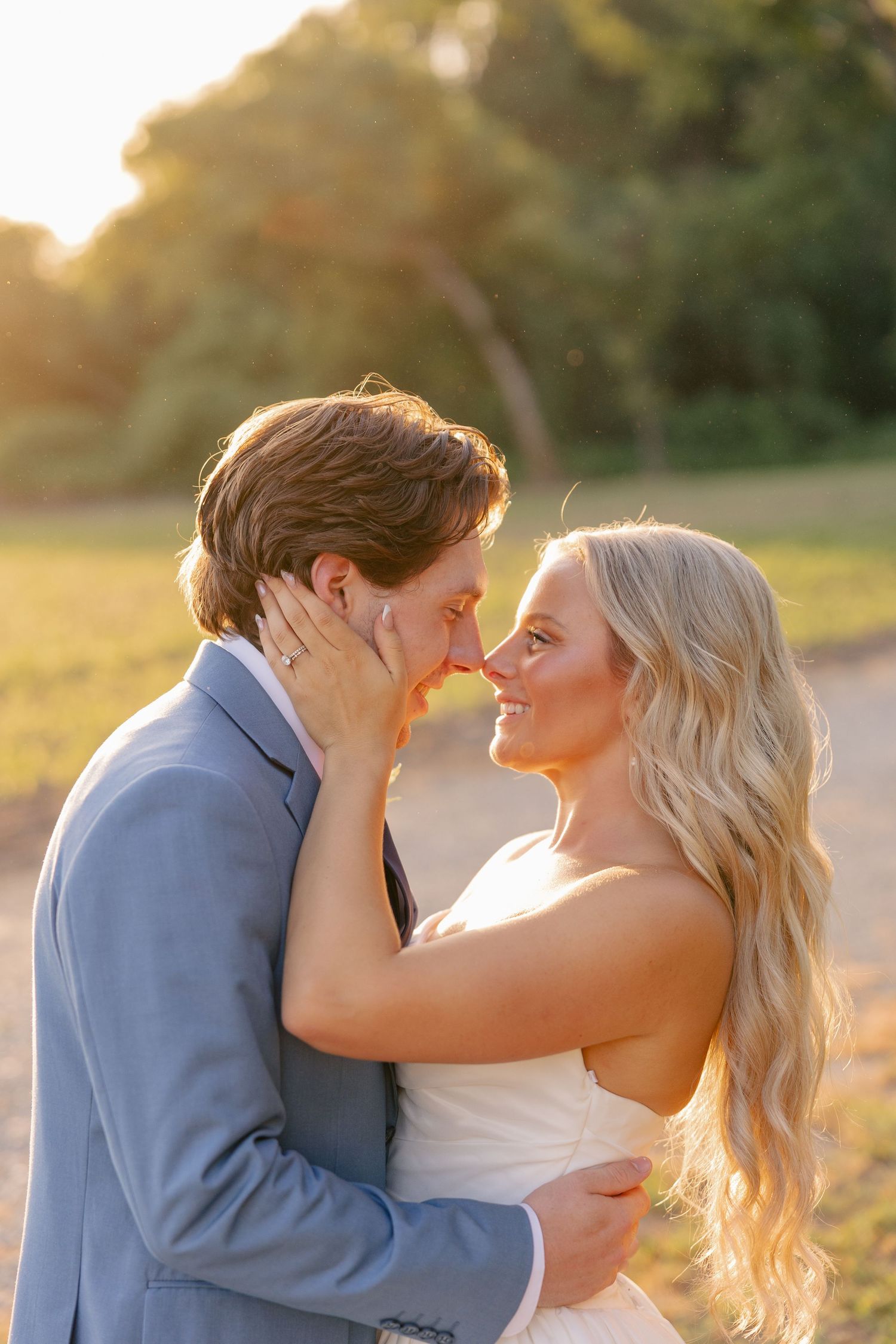 Bride and groom share a romantic almost-kiss at sunset, bathed in warm golden light outdoors.