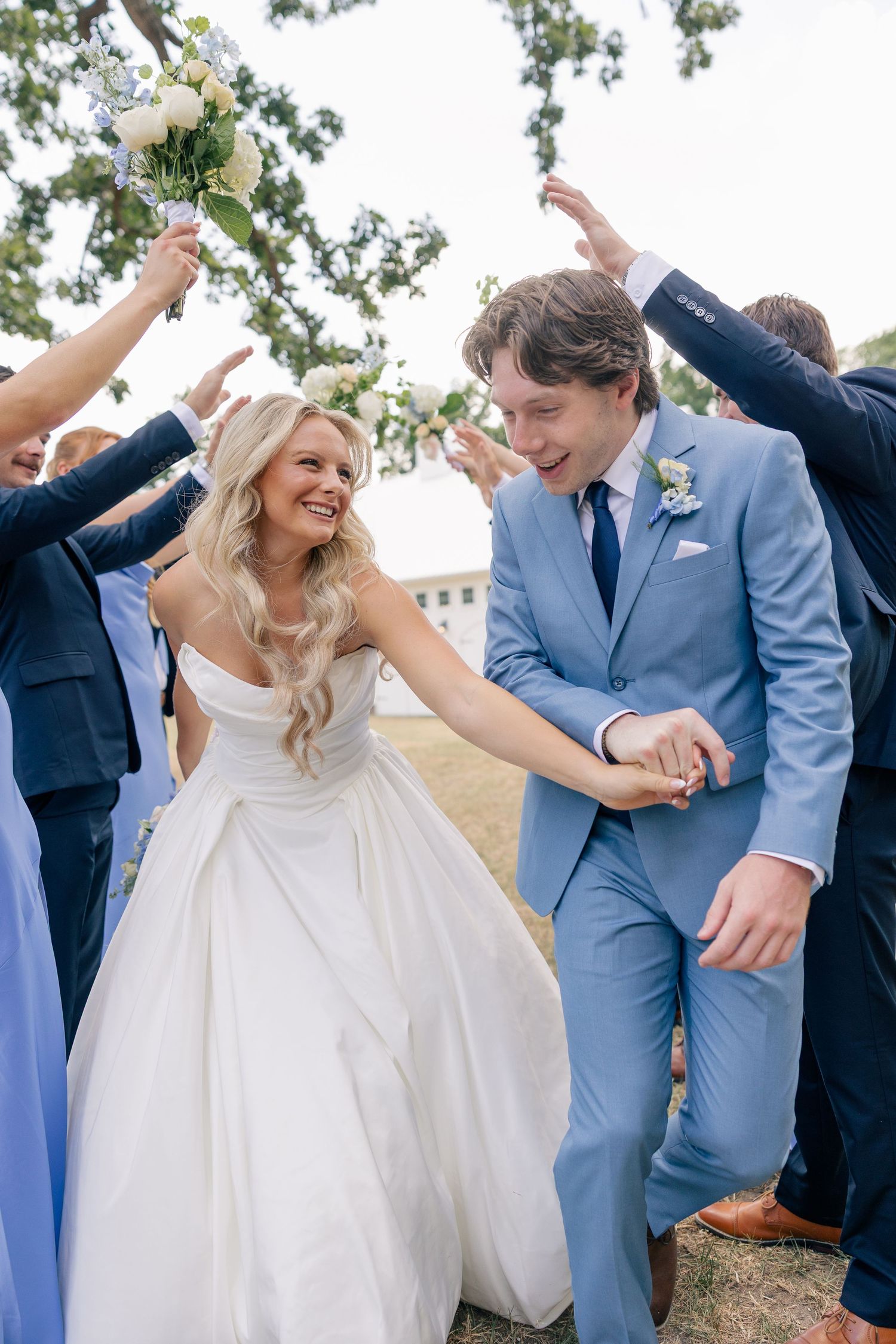 Smiling bride and groom walk through cheering wedding party after ceremony.