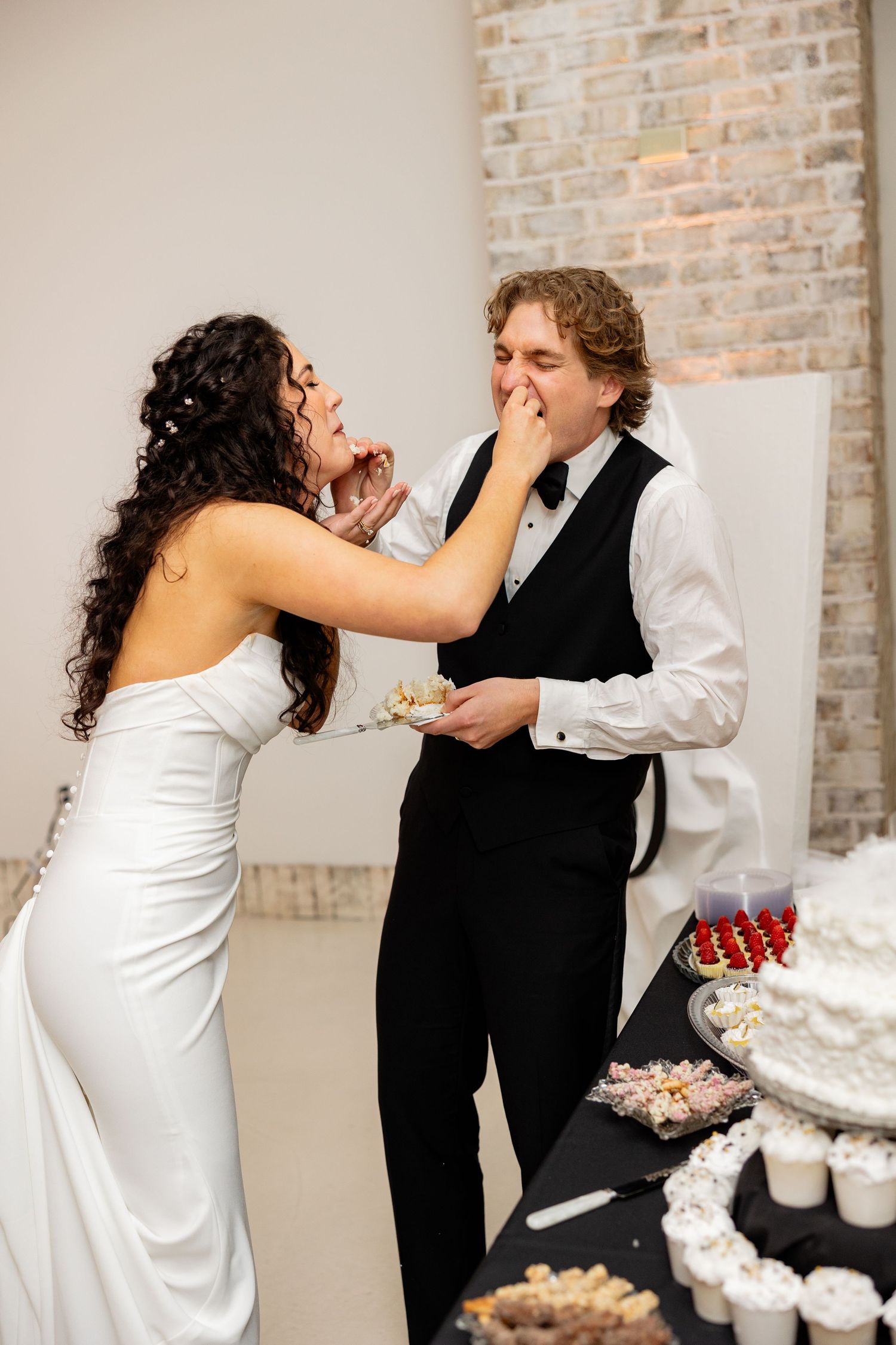 A couple laughing while feeding each other cake at their wedding reception.