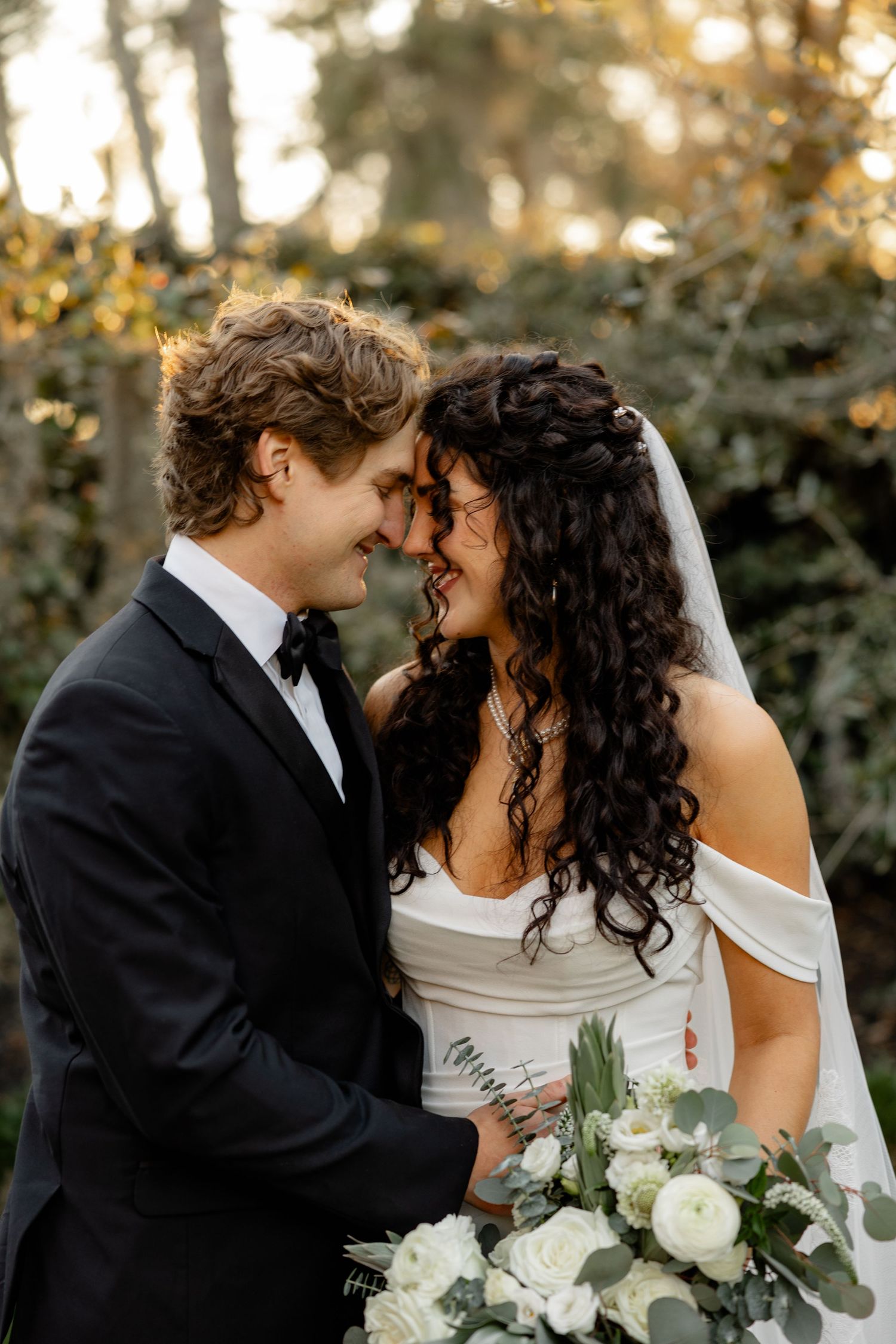 A romantic moment between newlyweds in a garden setting with a white floral bouquet.