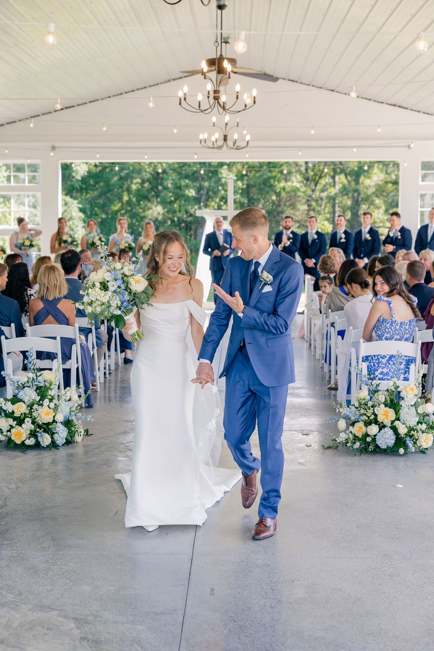 Newlyweds walk back down aisle smiling after wedding ceremony under white tent with flowers.