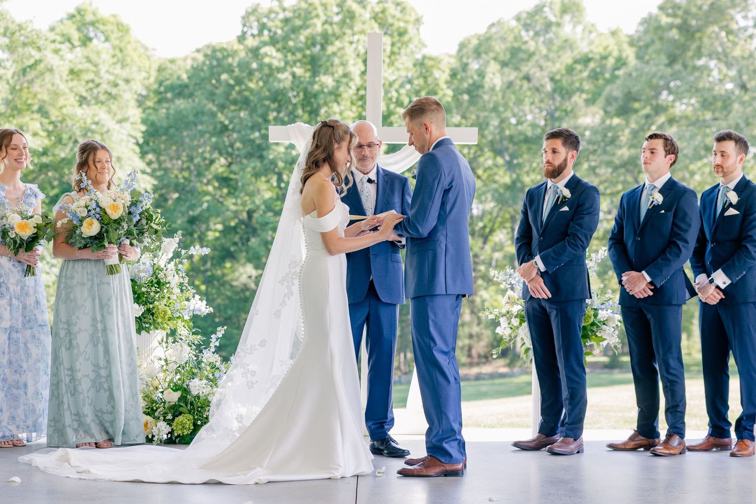 Bride and groom exchange vows at outdoor wedding ceremony before white cross altar.
