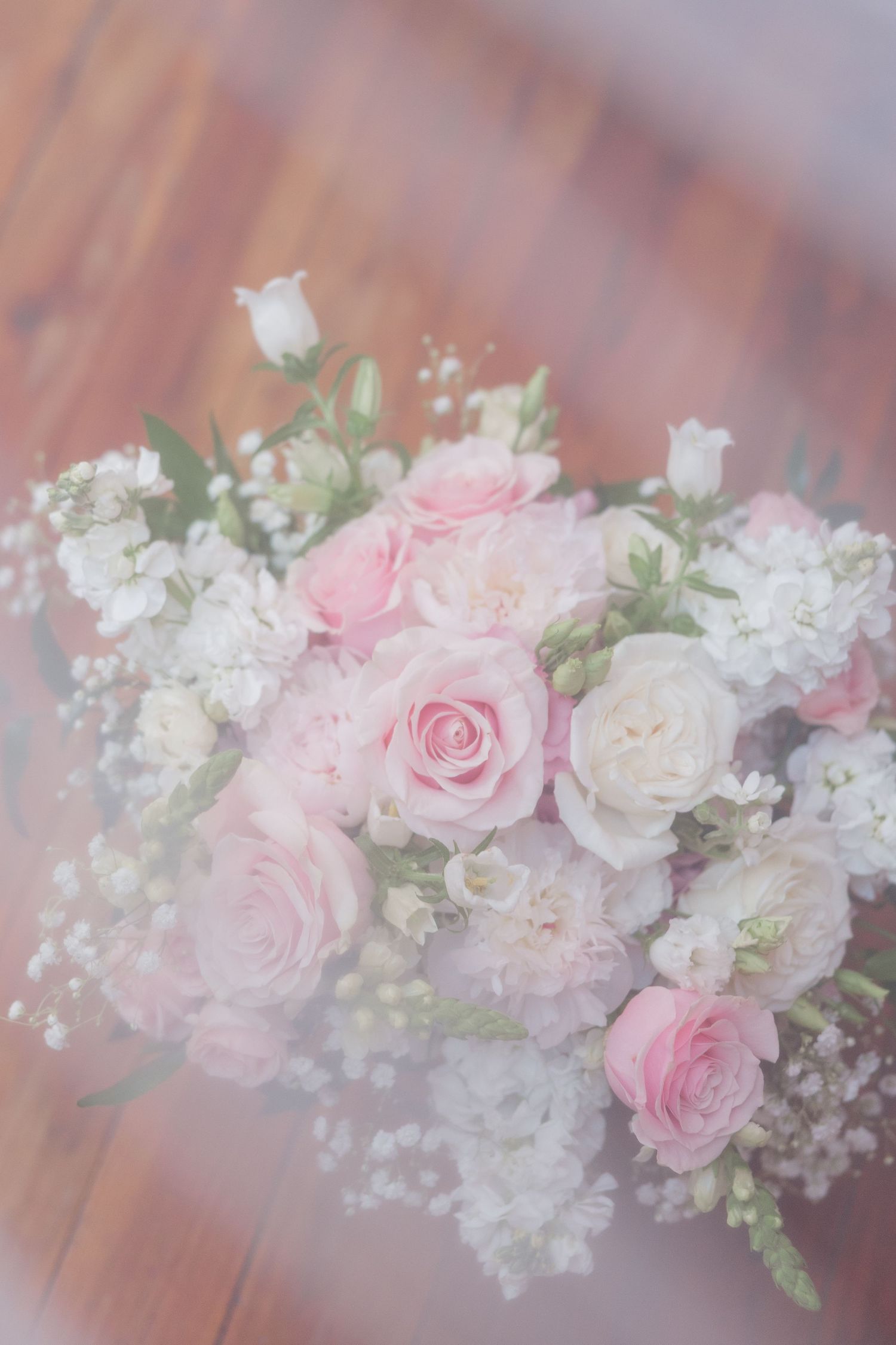 Delicate pink roses and white baby's breath flowers arranged in an elegant floral garland on a wooden surface.