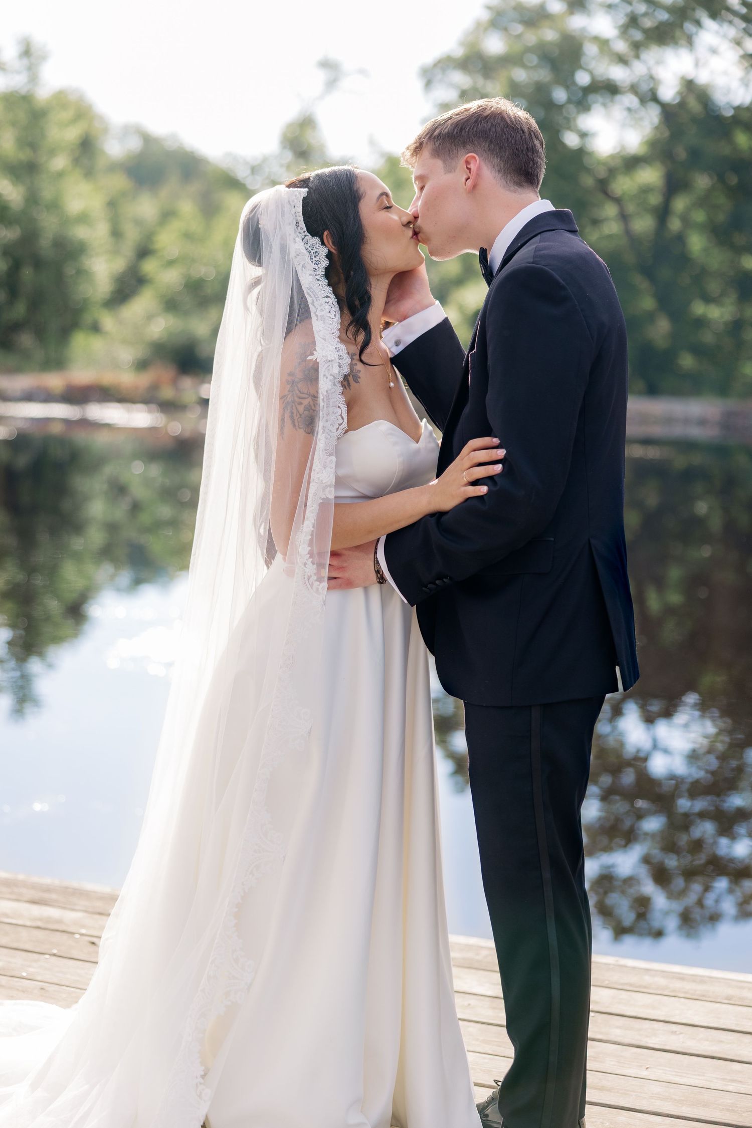 Romantic wedding couple shares intimate moments on a wooden dock by a serene lake.