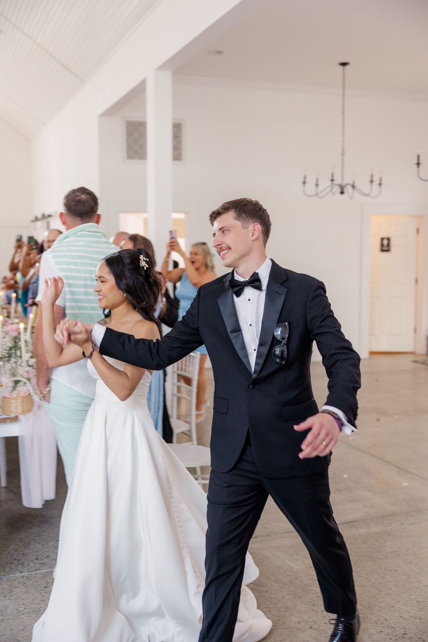 Wedding party dancing and celebrating in a bright white indoor venue.
