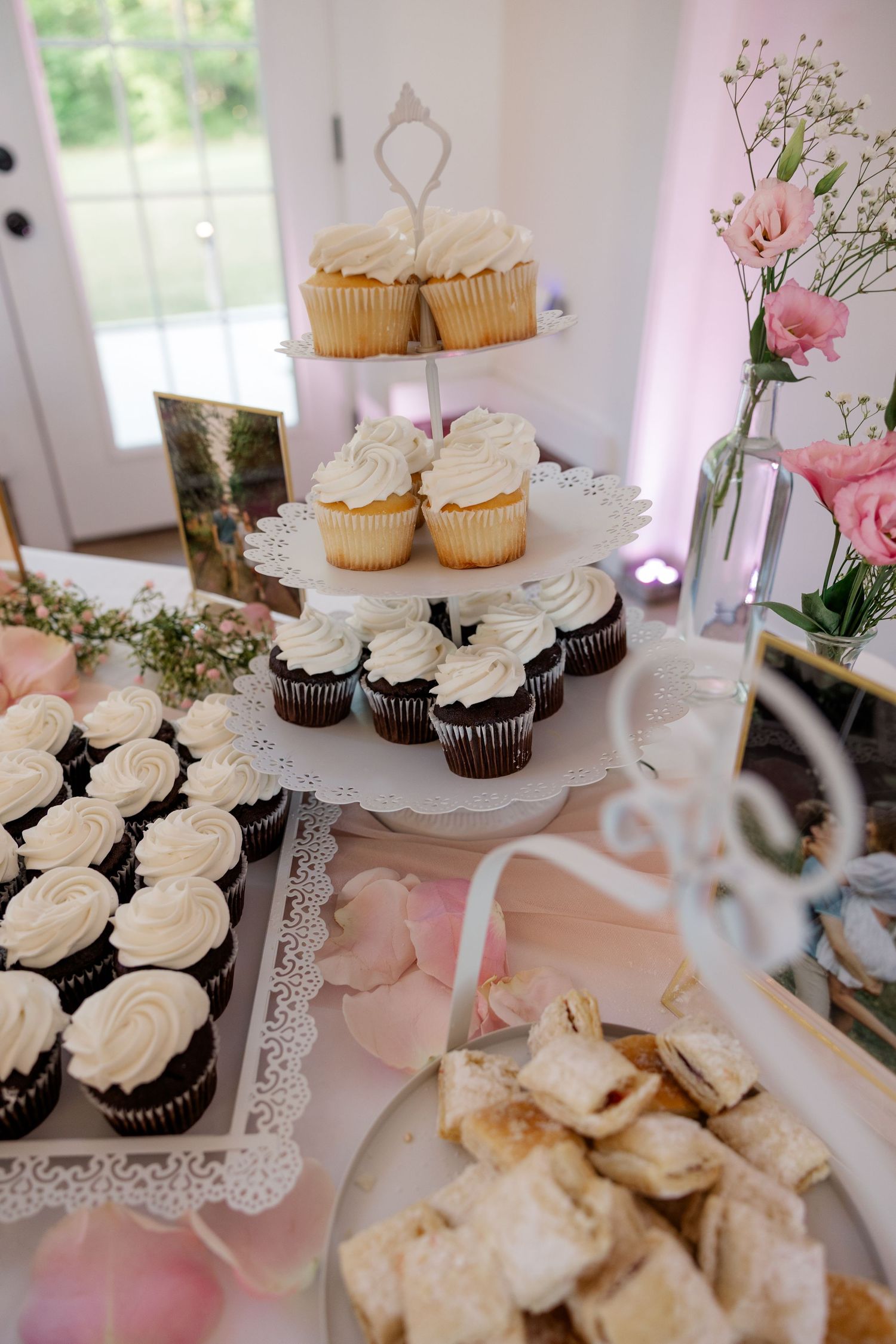 Wedding dessert table with white cupcakes and pink floral decorations displayed on lace doilies.