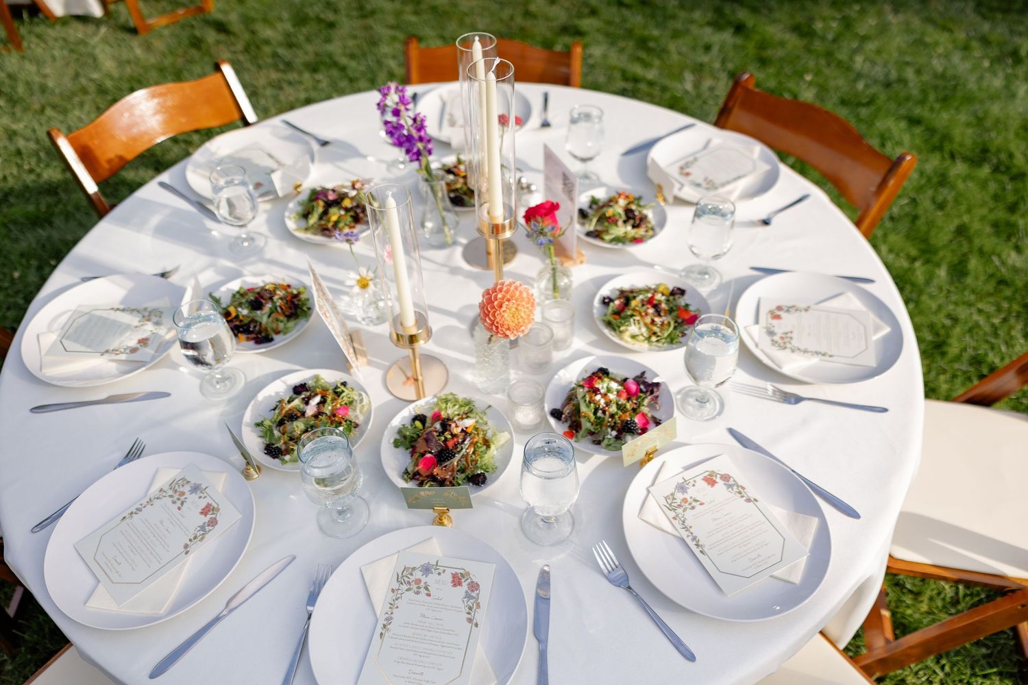 Elegant white table settings at an outdoor wedding reception with floral centerpieces.