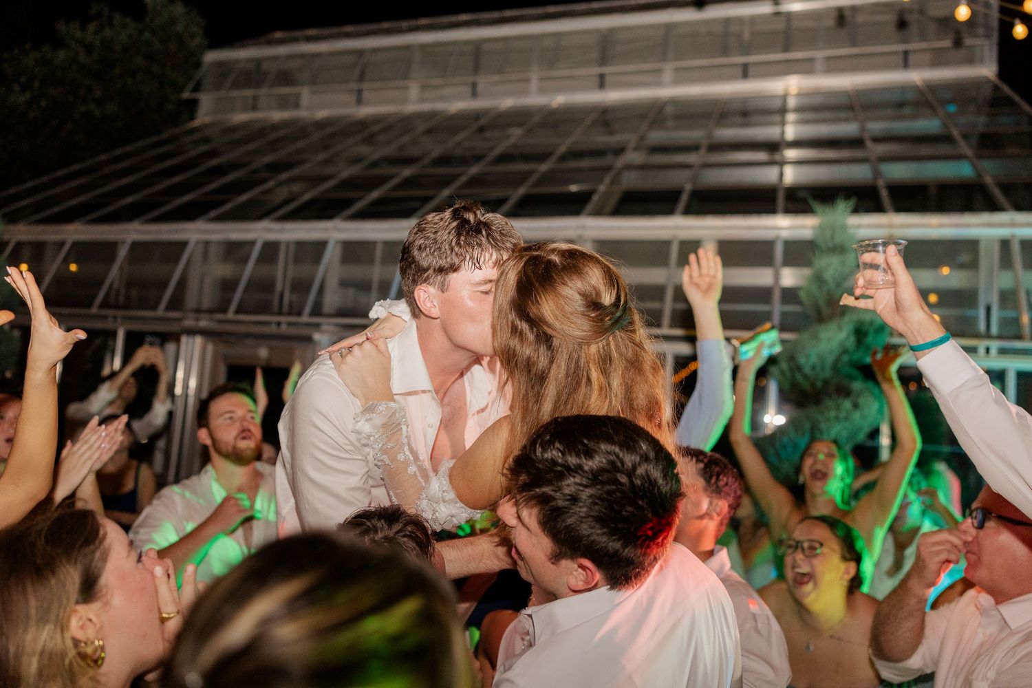 Wedding reception dance floor filled with energetic guests celebrating under evening lights.