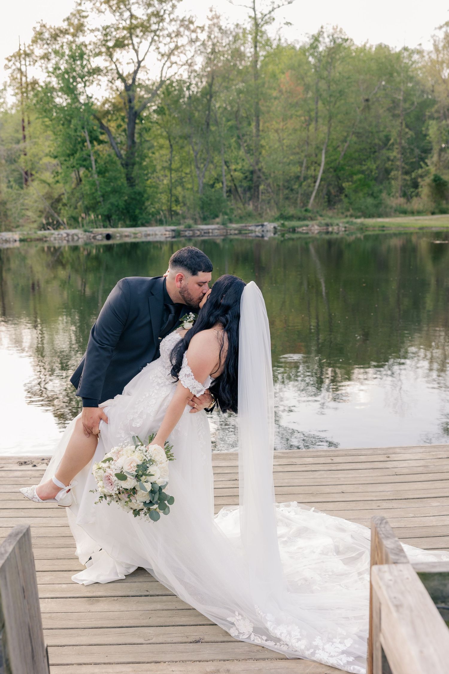 A romantic wedding photo on a dock with the couple sharing an intimate moment over a lake.