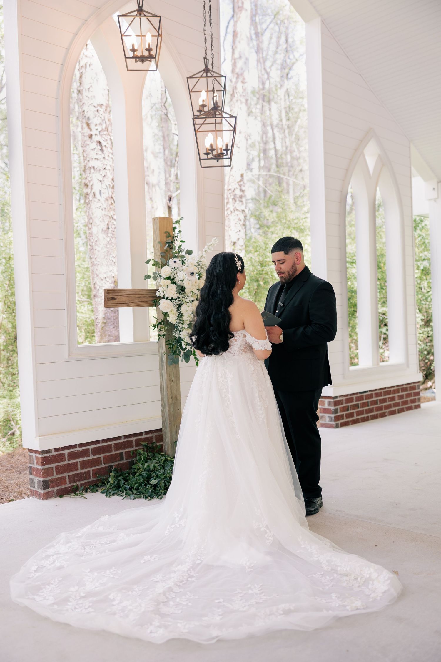 Romantic wedding portraits under white arched colonnade with hanging lanterns and beautiful landscaping.
