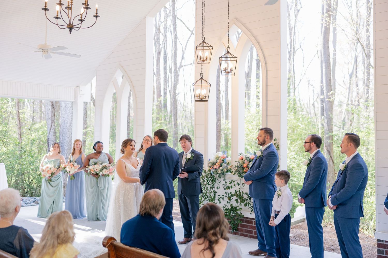 Wedding ceremony setup in a bright white venue with chandelier and wooden beams.