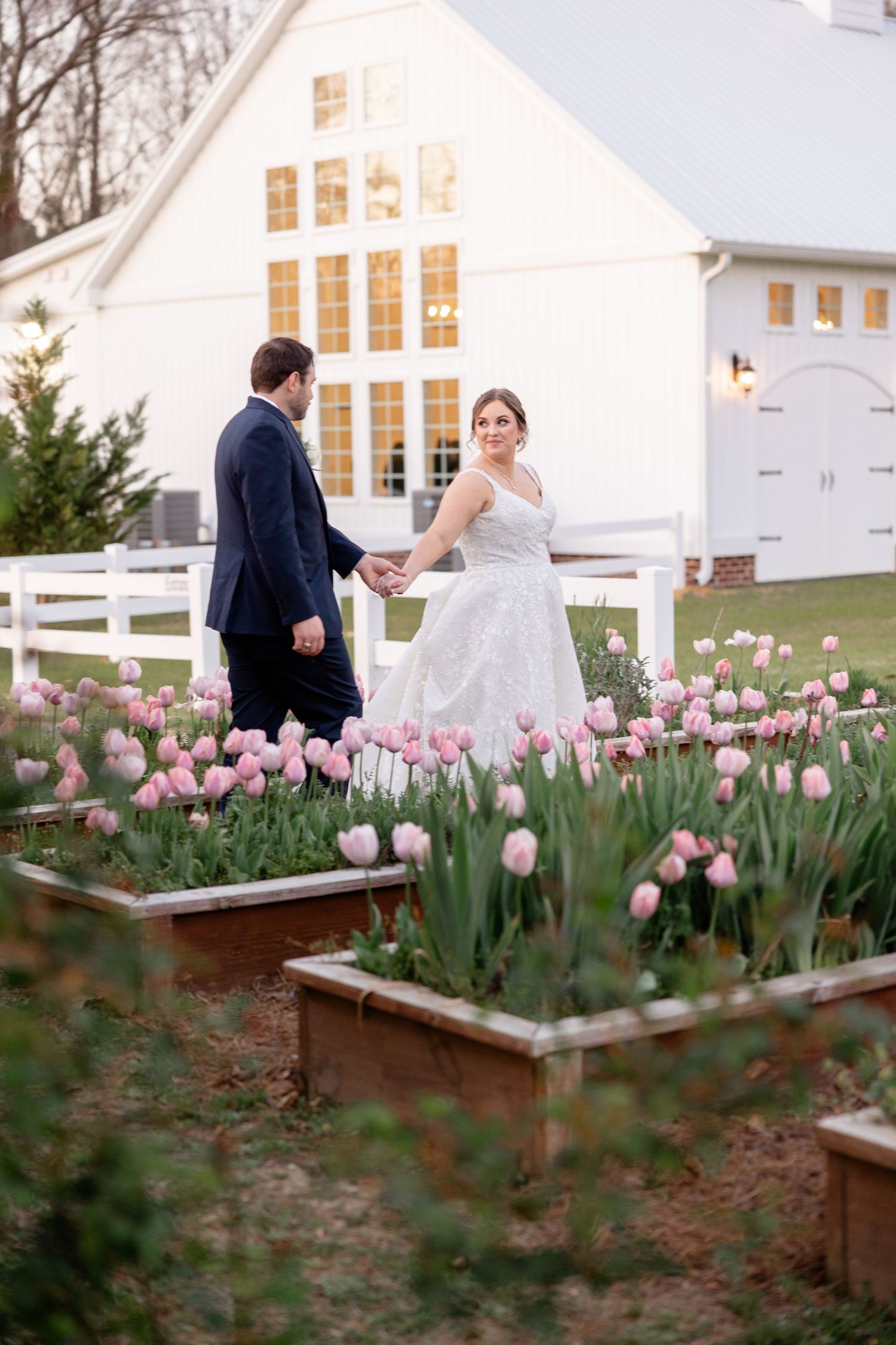 White farmhouse with pink tulip garden beds in full spring bloom.