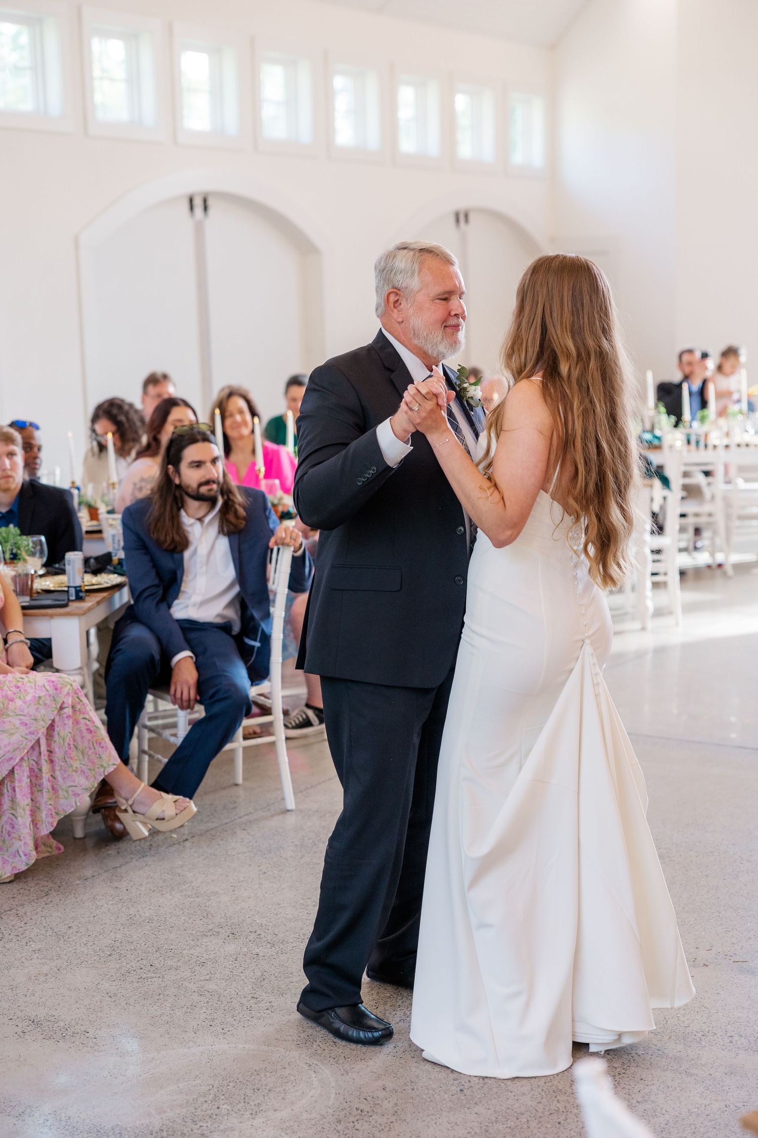 Wedding guests dance under bright white ceiling lights in spacious indoor reception venue.