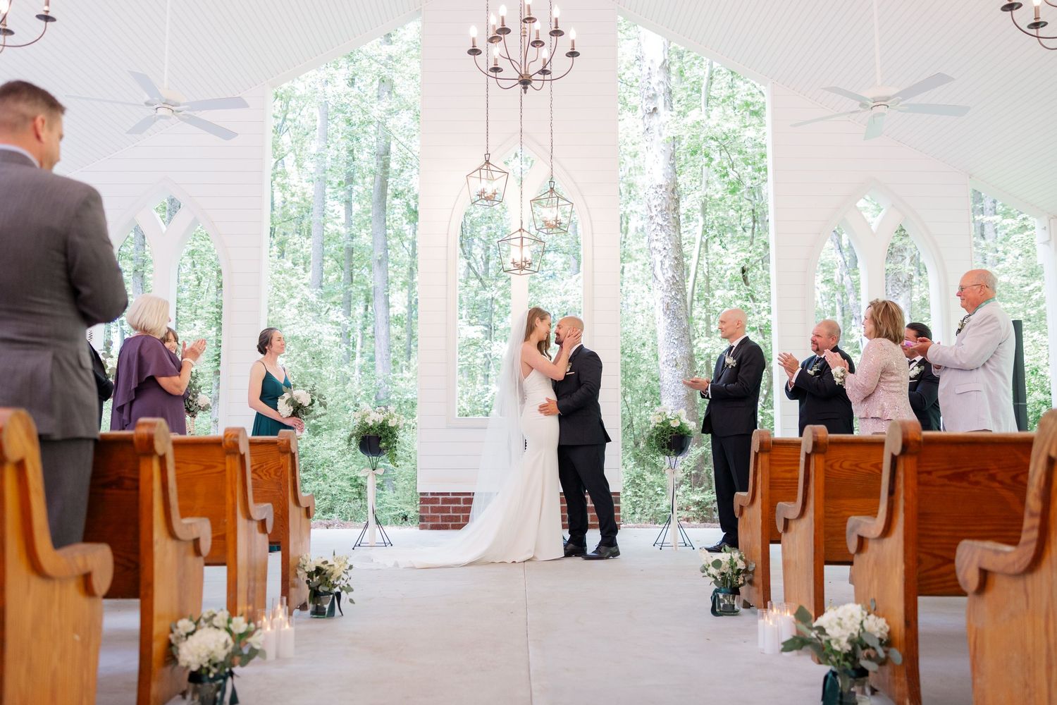 Wedding ceremony in a bright chapel with wooden pews and natural light streaming through windows.