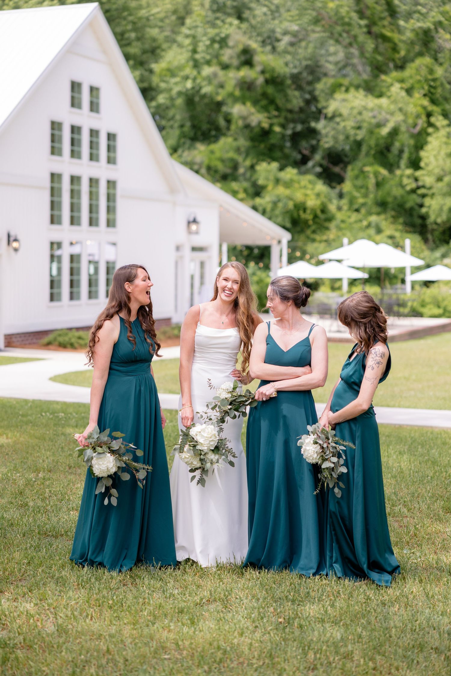 Bridesmaids in teal dresses share candid moment during outdoor wedding photoshoot.