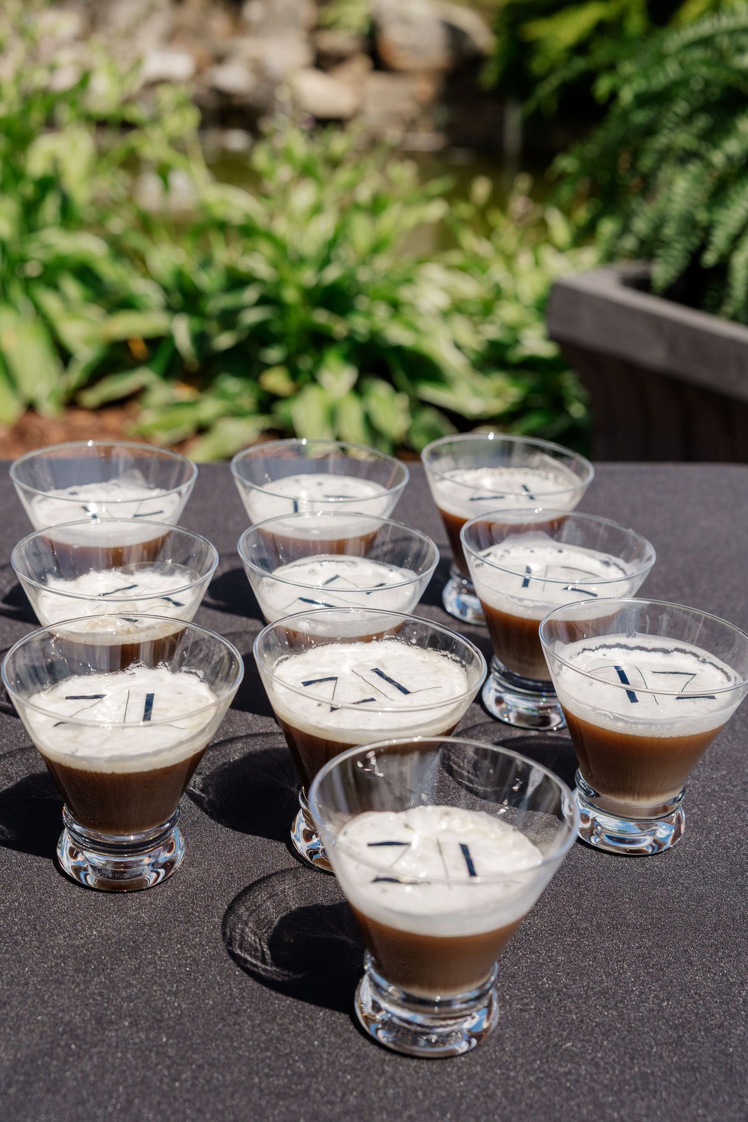Several martini glasses filled with layered espresso cocktails arranged on a dark surface outdoors.