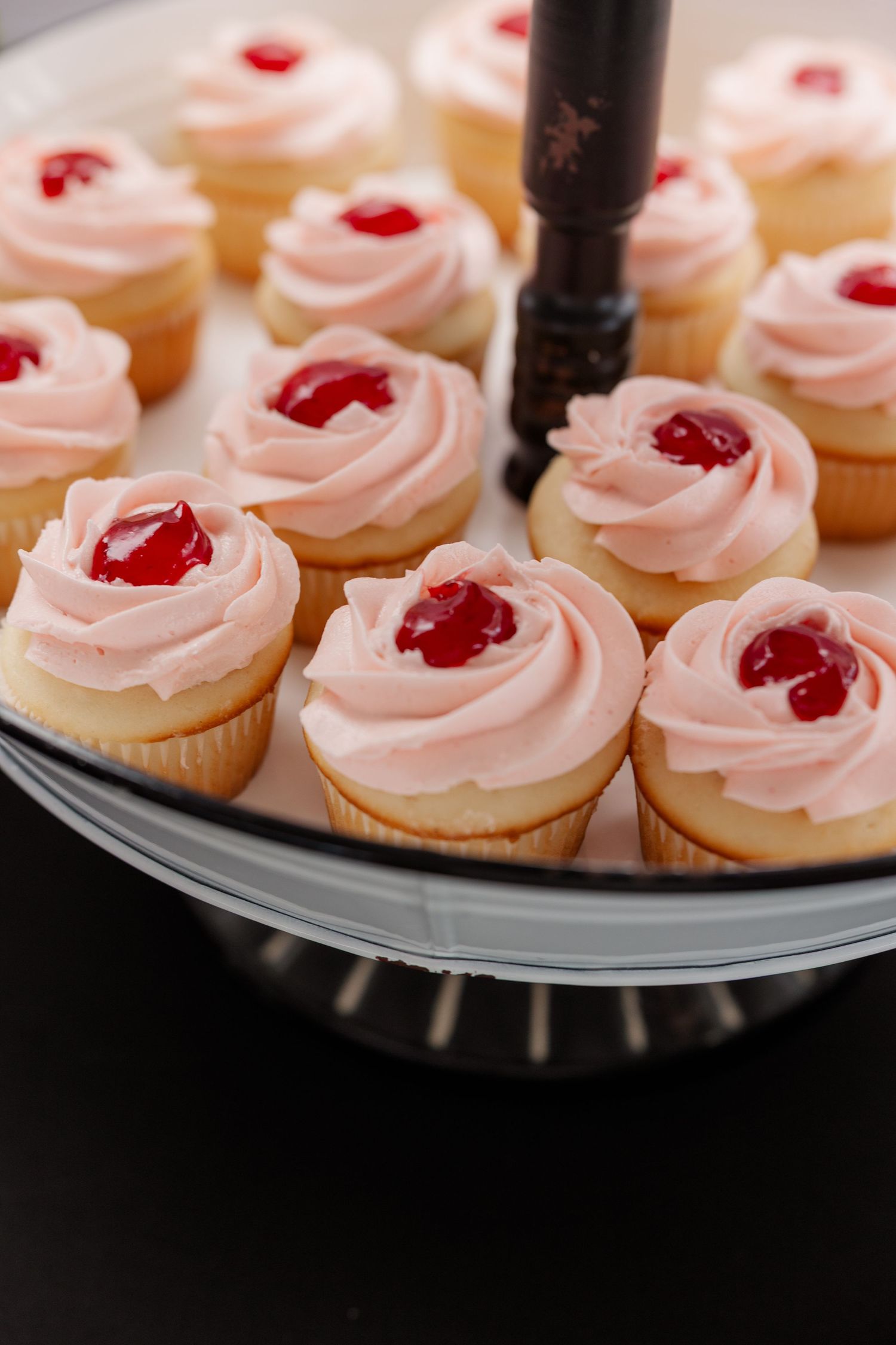 Pink frosted mini cupcakes topped with cherry garnishes arranged on a dark serving platter.