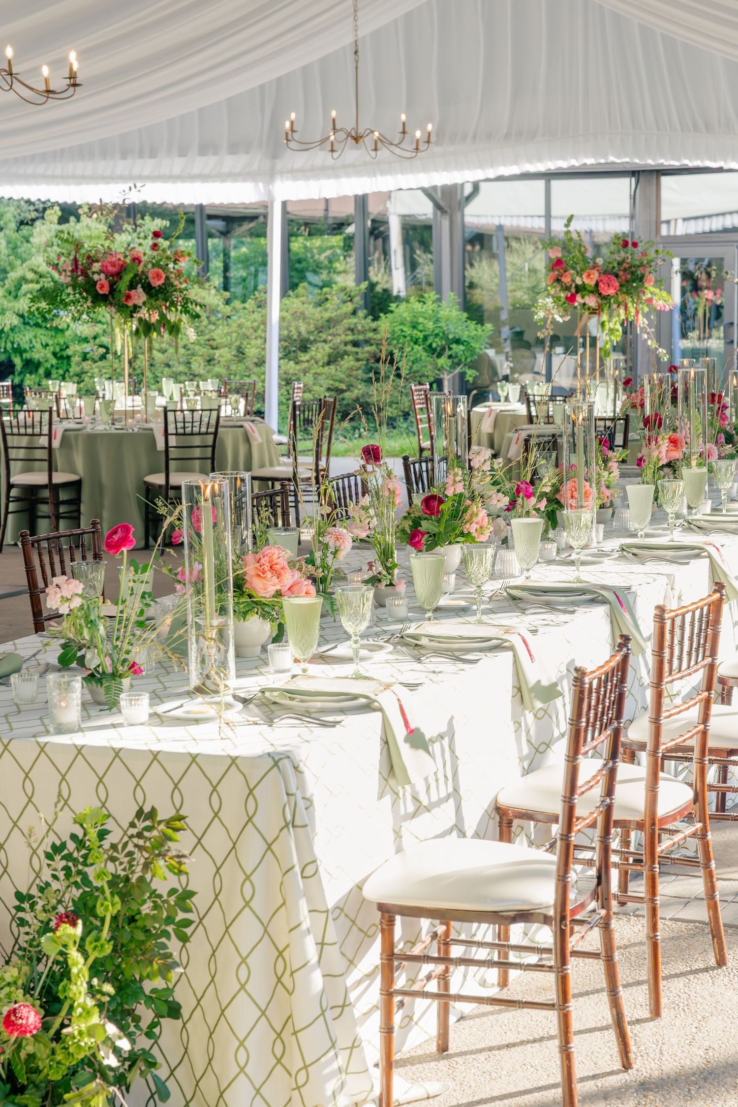 Wedding reception tent with long head table adorned with pink floral arrangements and chiavari chairs.
