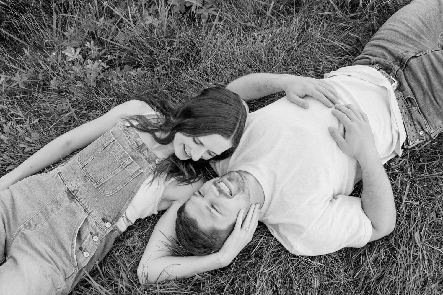 A couple lies together on grass in a tender black and white moment.