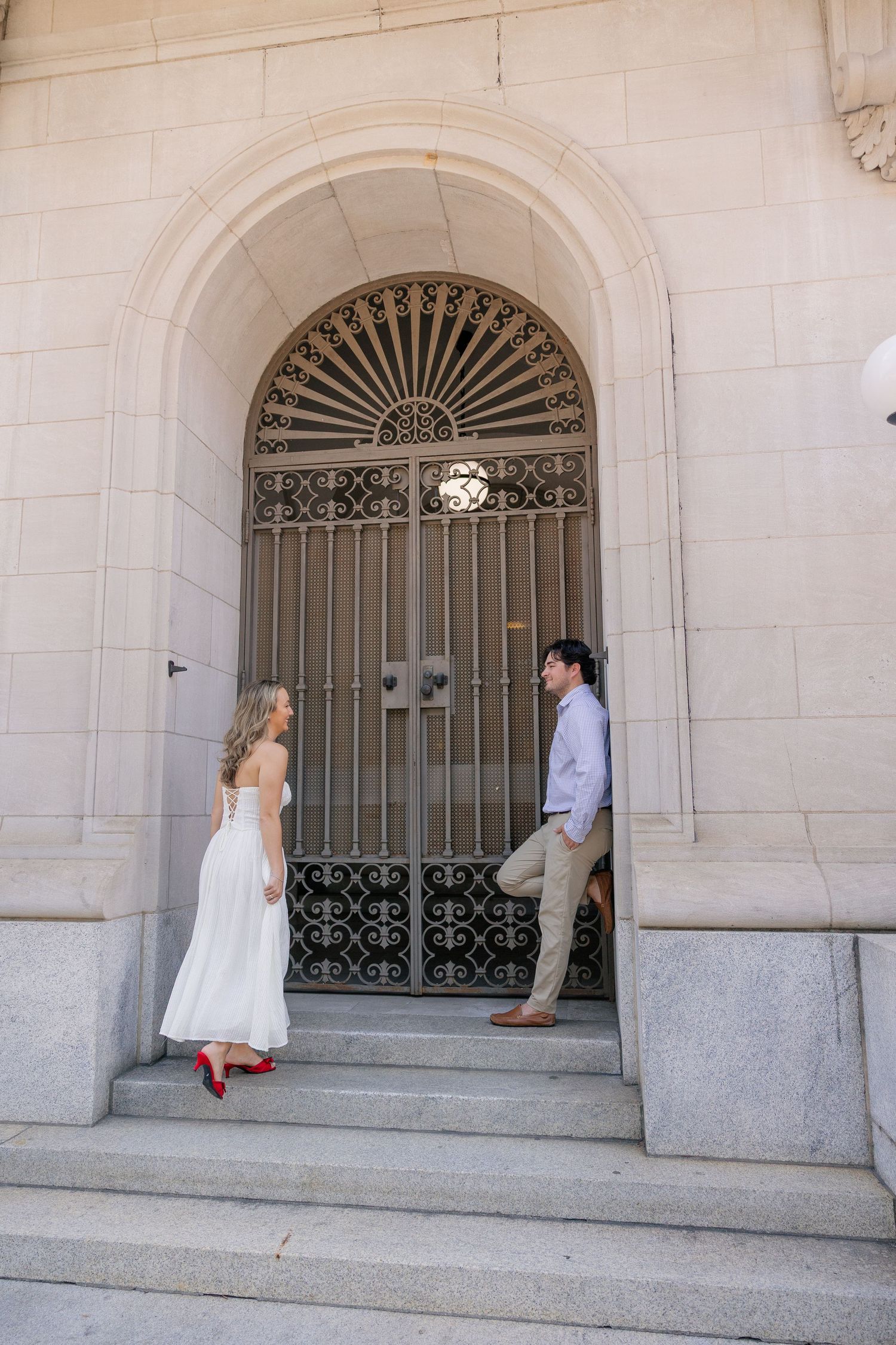 Couple sharing a romantic moment on stone steps by an ornate arched iron gate door.