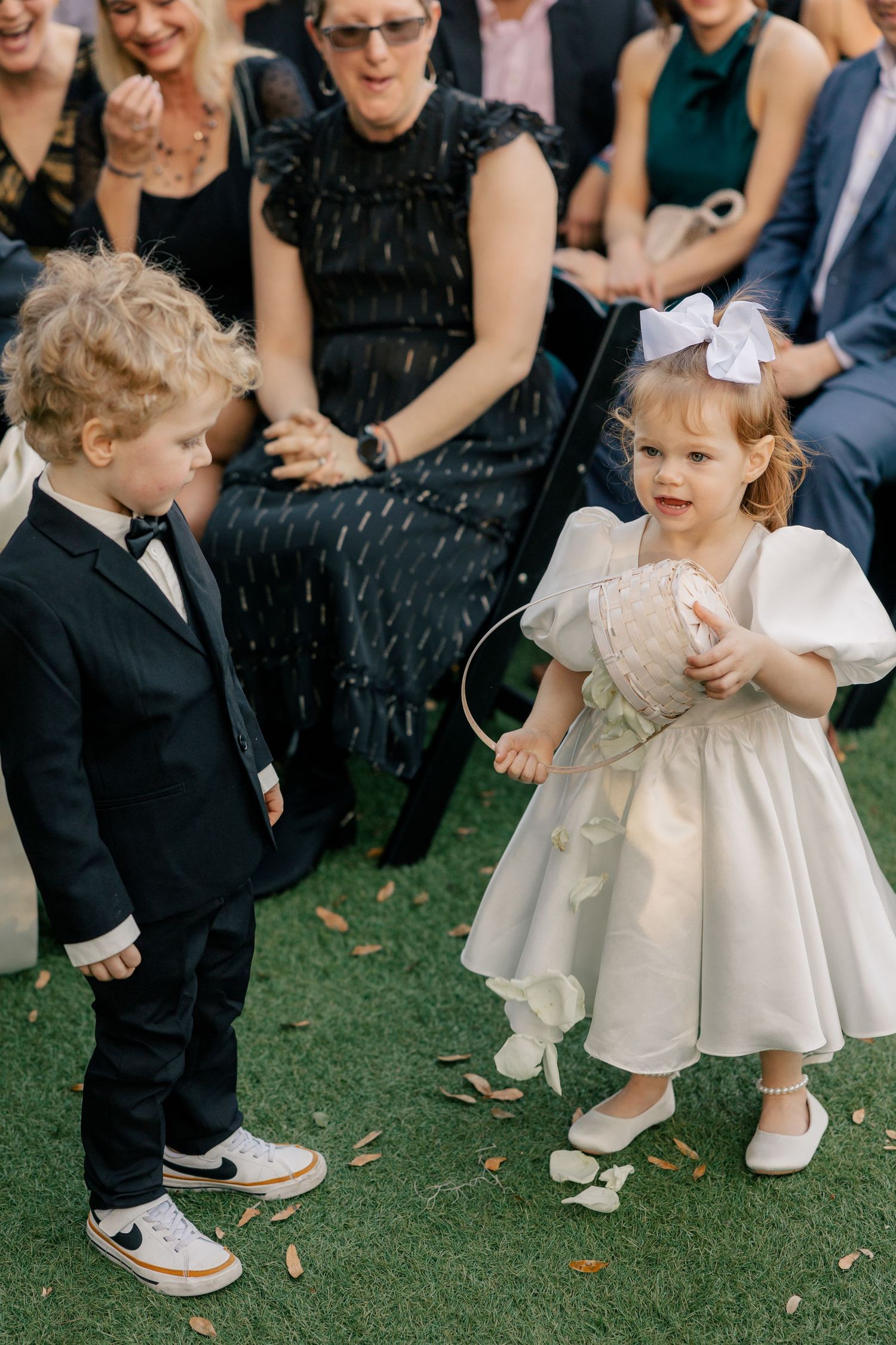 Two adorably dressed young children interacting joyfully at a formal outdoor event.