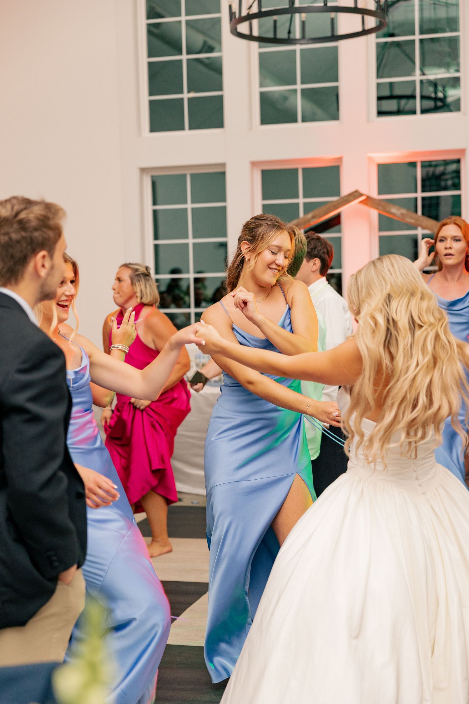 Bridesmaids in blue satin dresses dancing with bride in white gown at wedding reception.