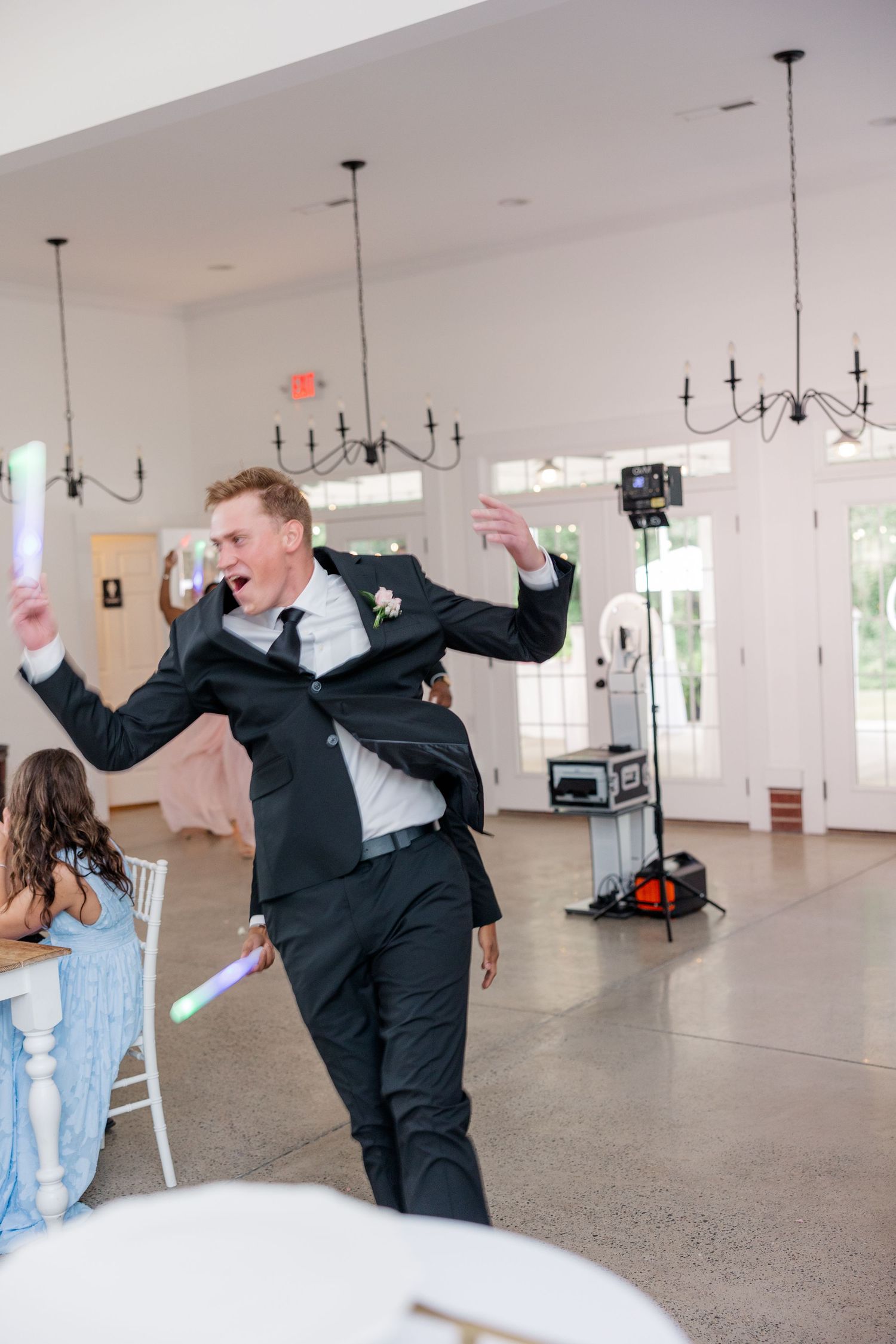 A joyful celebration at a wedding reception with energetic dancing in a bright indoor venue with pendant lights.