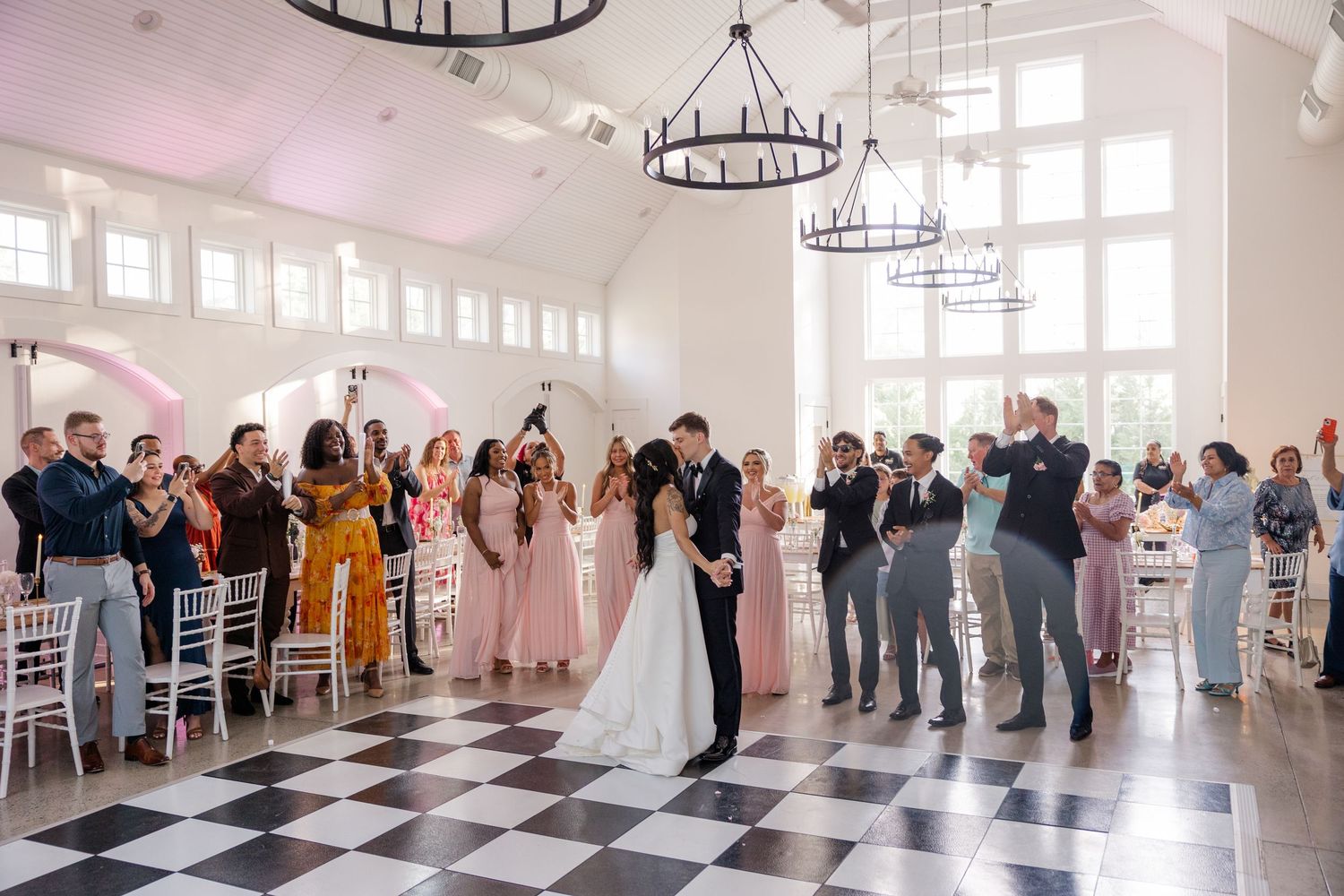 Wedding reception celebration on checkered floor with guests clapping.