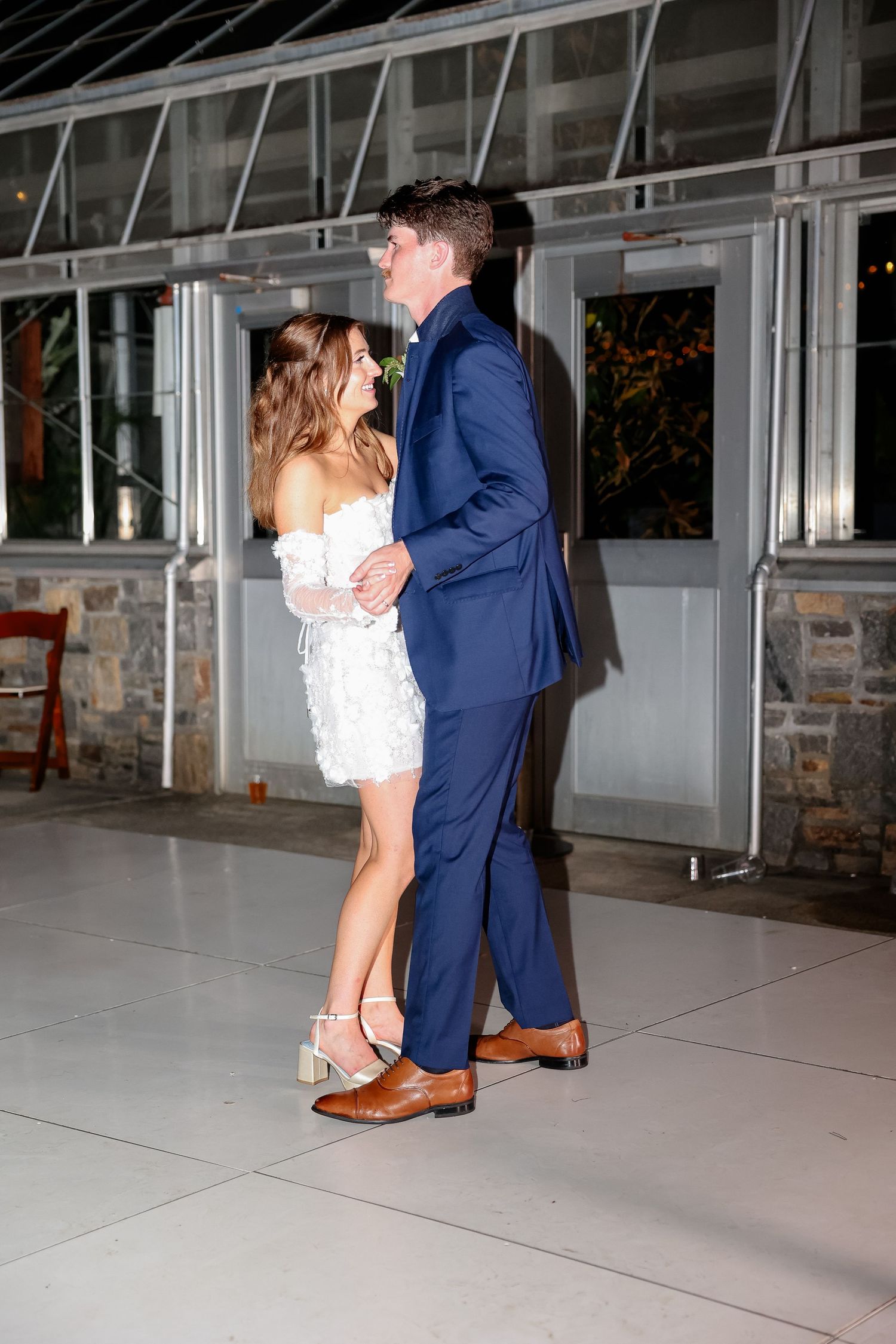 A wedding couple dancing together on a sleek indoor floor with windows behind them.