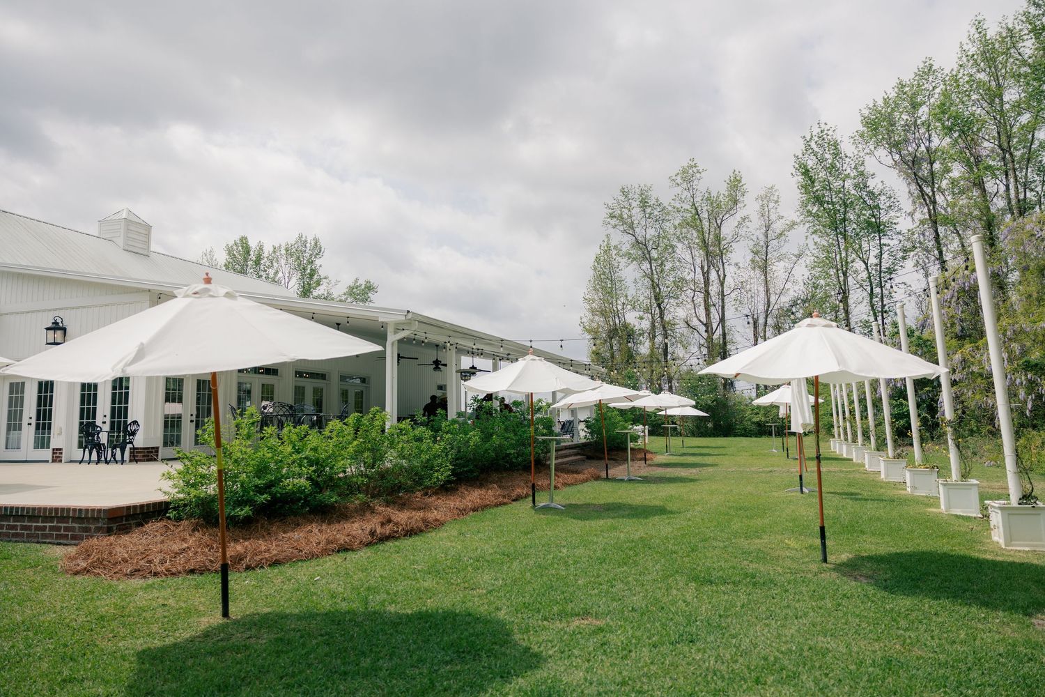 Panoramic view of a white wedding venue surrounded by green landscaping and tall trees.
