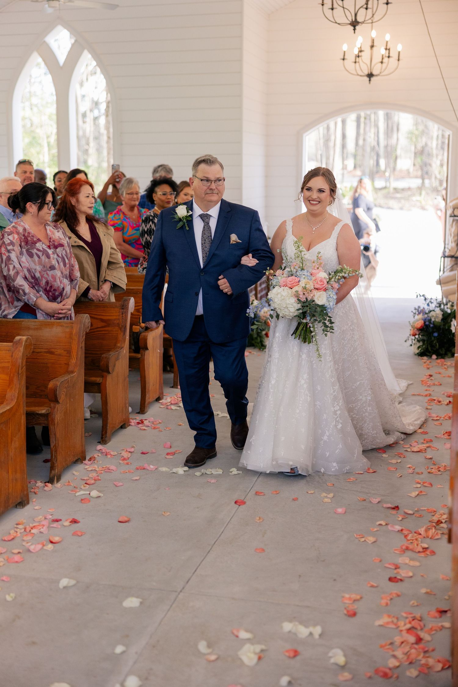 Wedding couple walks down church aisle covered in scattered rose petals.
