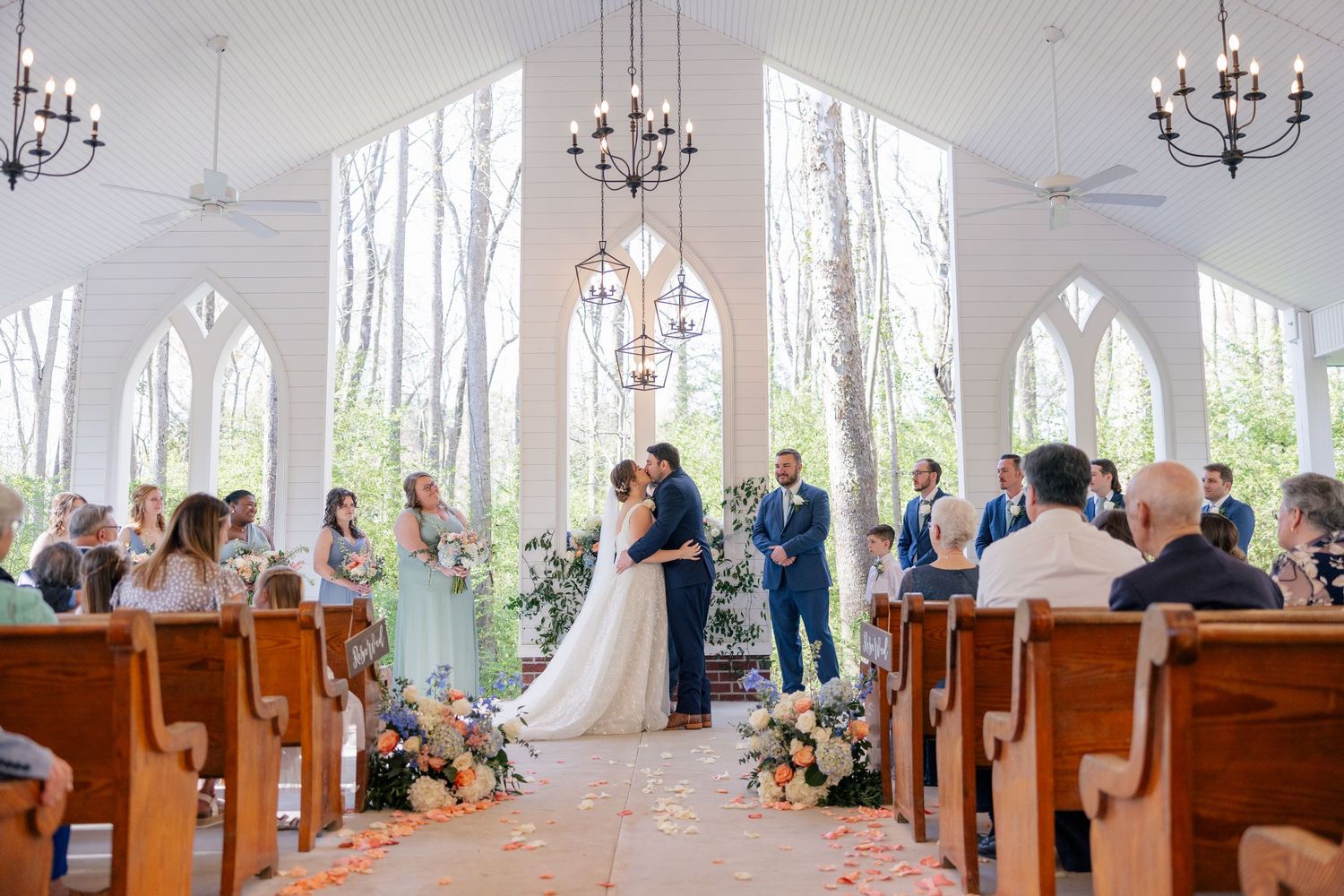 Panoramic view of a wedding ceremony in a bright chapel with natural woodland backdrop.