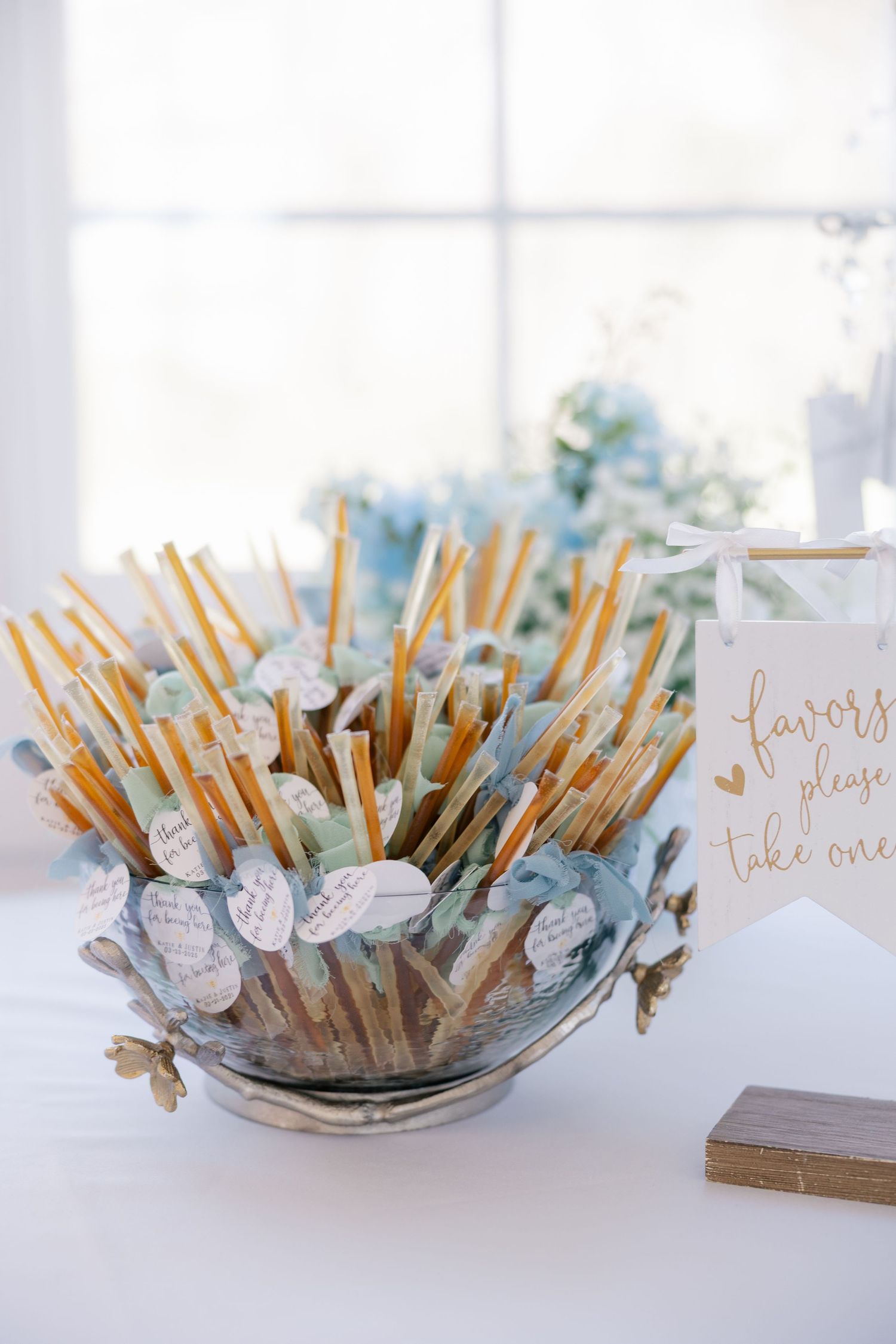Wedding favor display featuring wooden honey dippers with delicate blue ribbons and 'take one' signage.