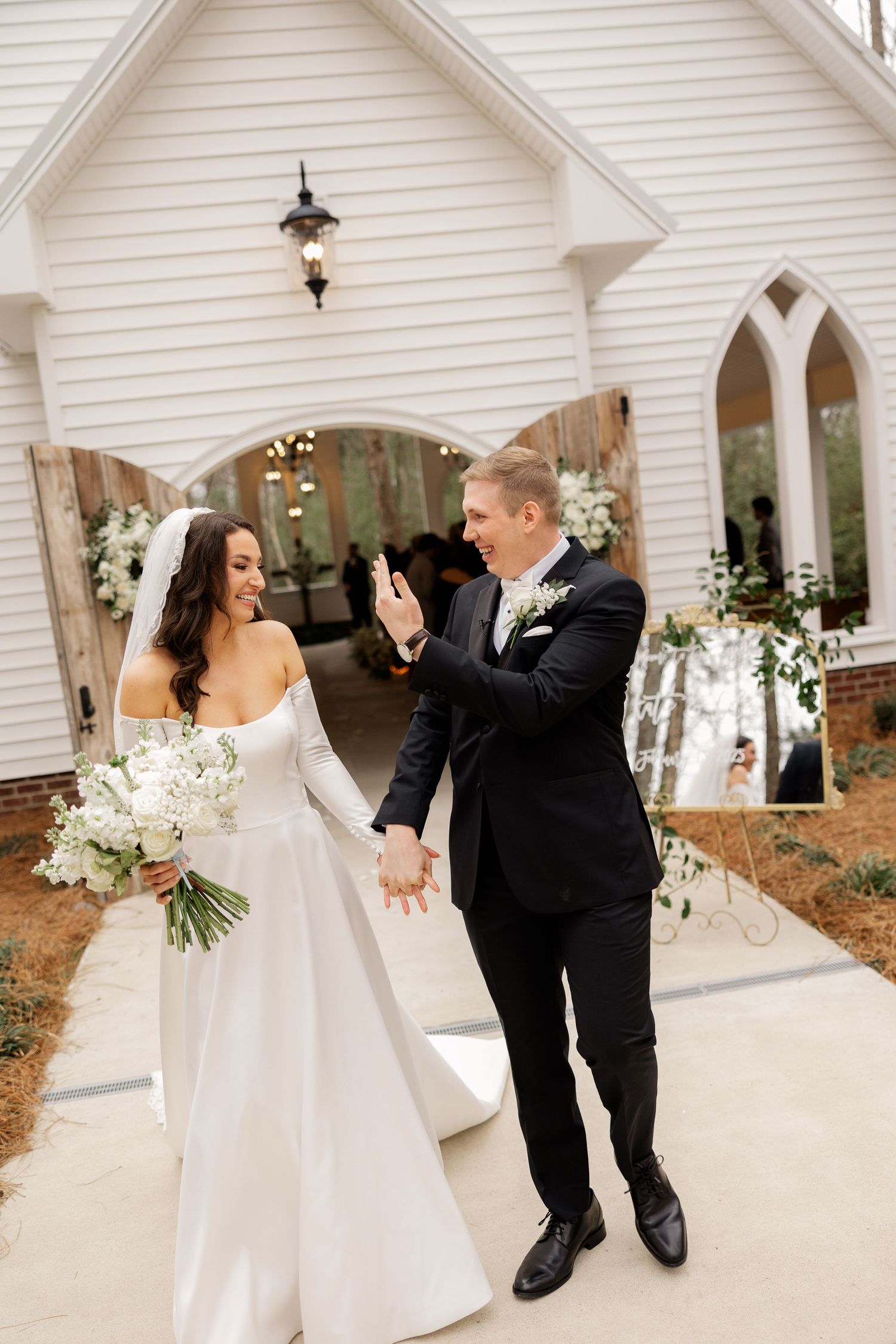 A joyful couple twirls and dances together outside a white chapel wedding venue.