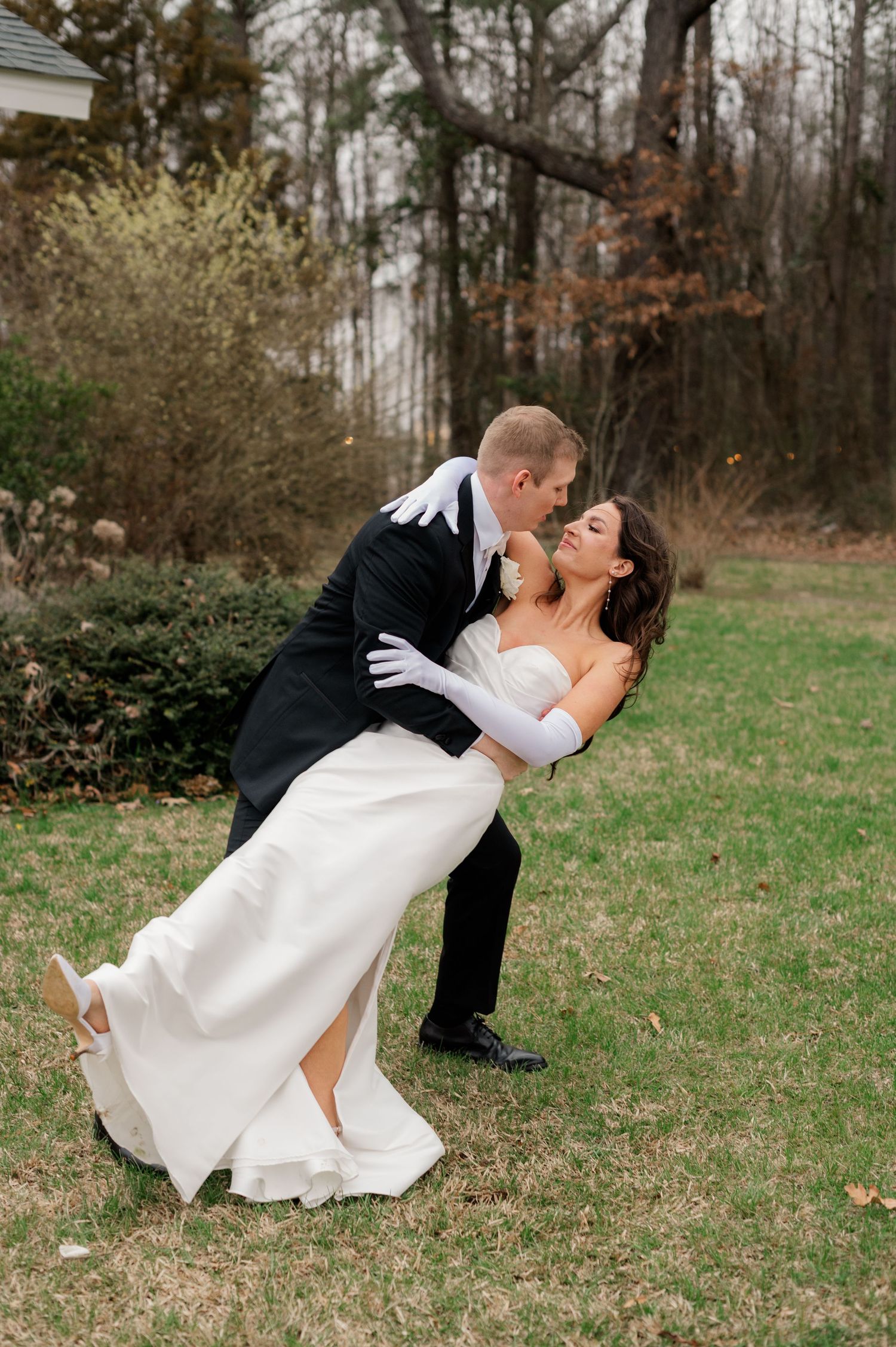 Romantic wedding couple performs dance dip pose on grassy lawn during photo session.