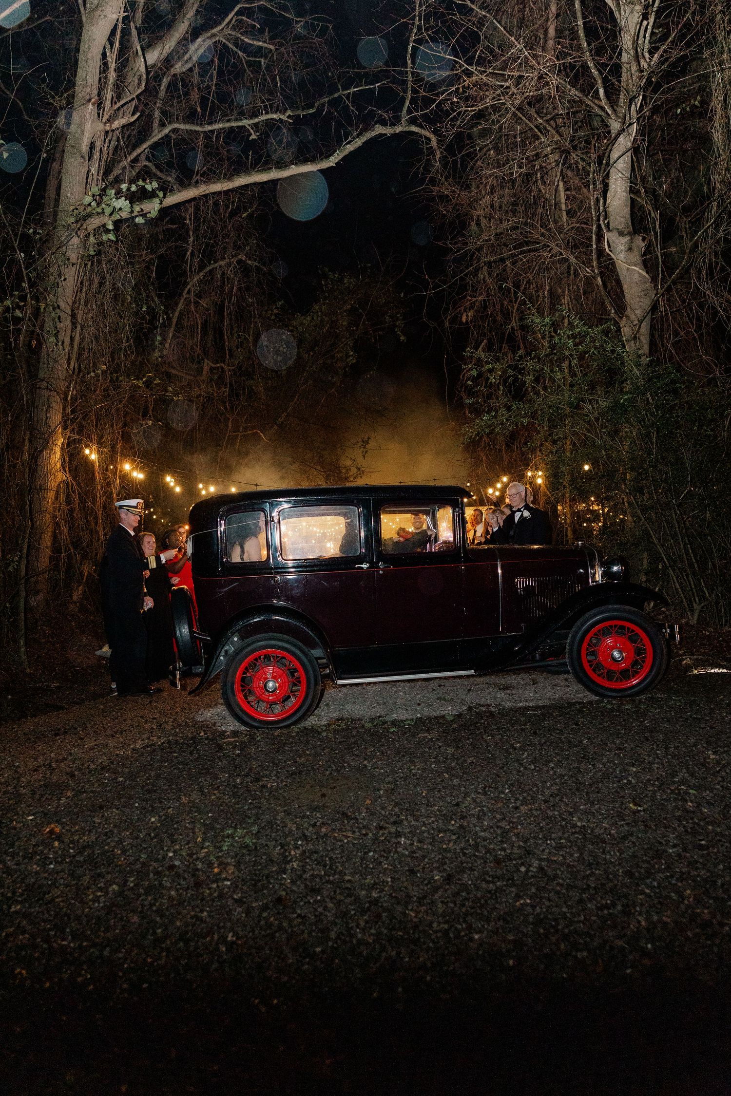 Vintage car with red wheels parked outside during nighttime wedding festivities.
