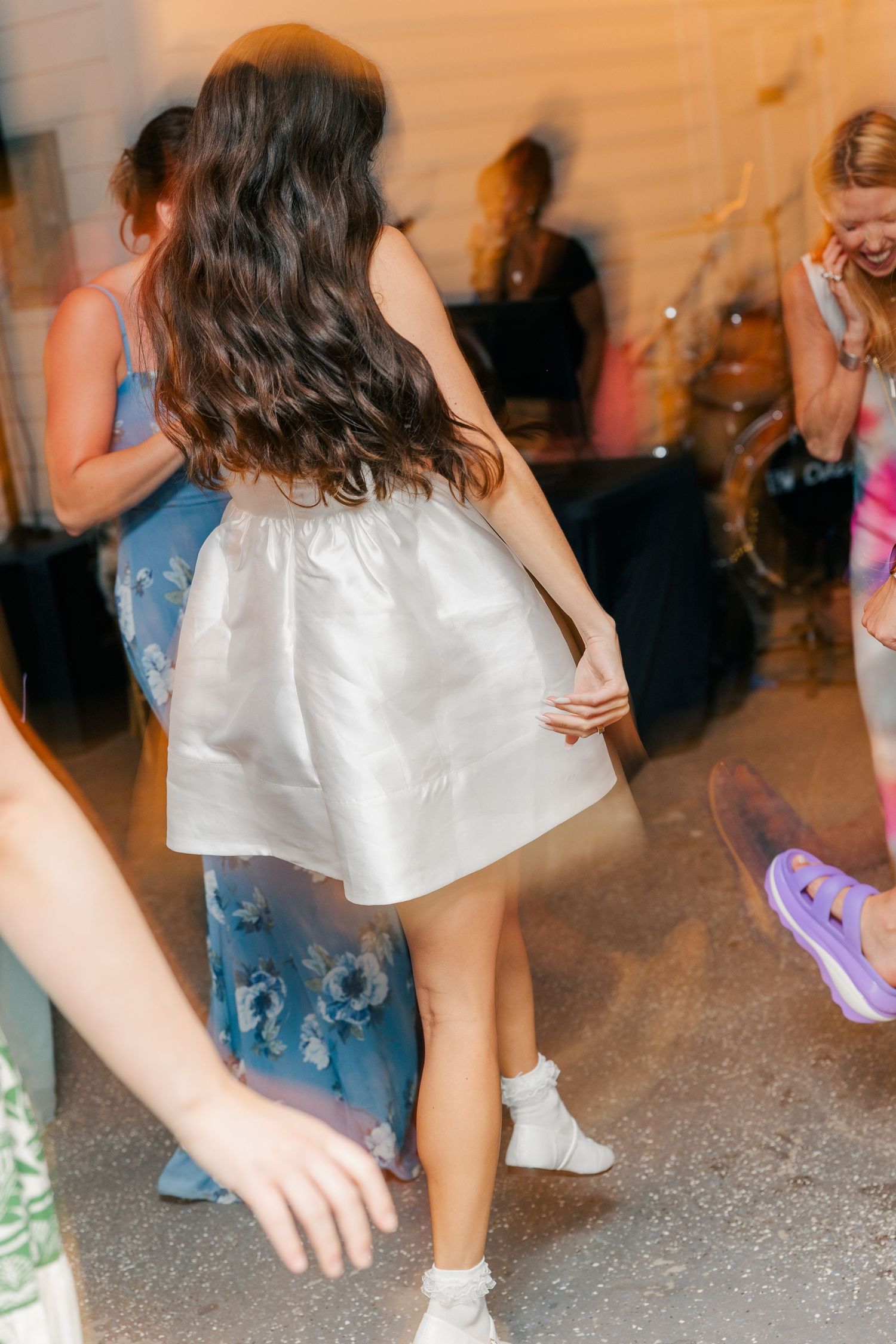 People dancing at a party, with someone wearing a white dress twirling on the dance floor.