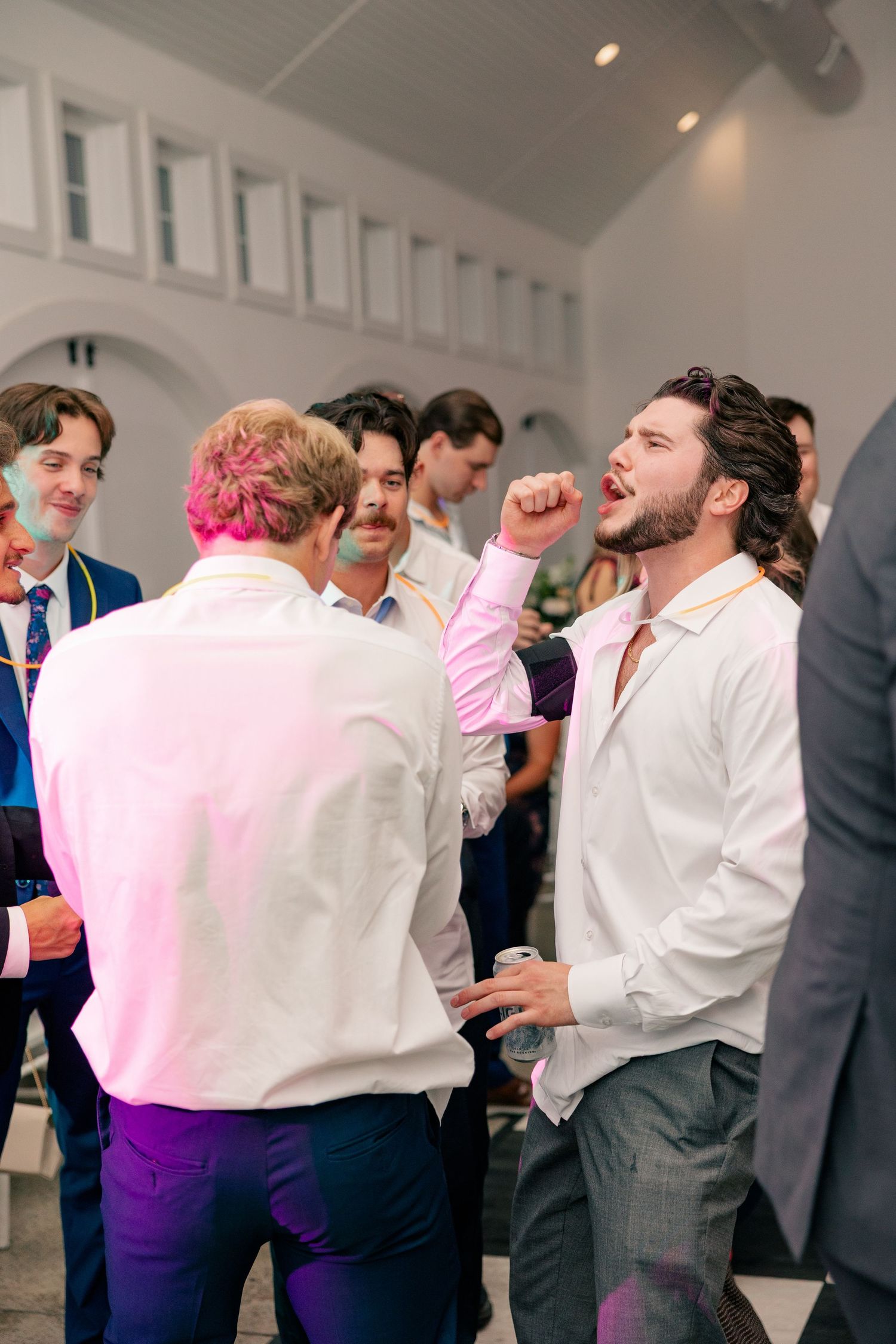 Men in dress shirts celebrating and dancing energetically at a lively wedding reception.