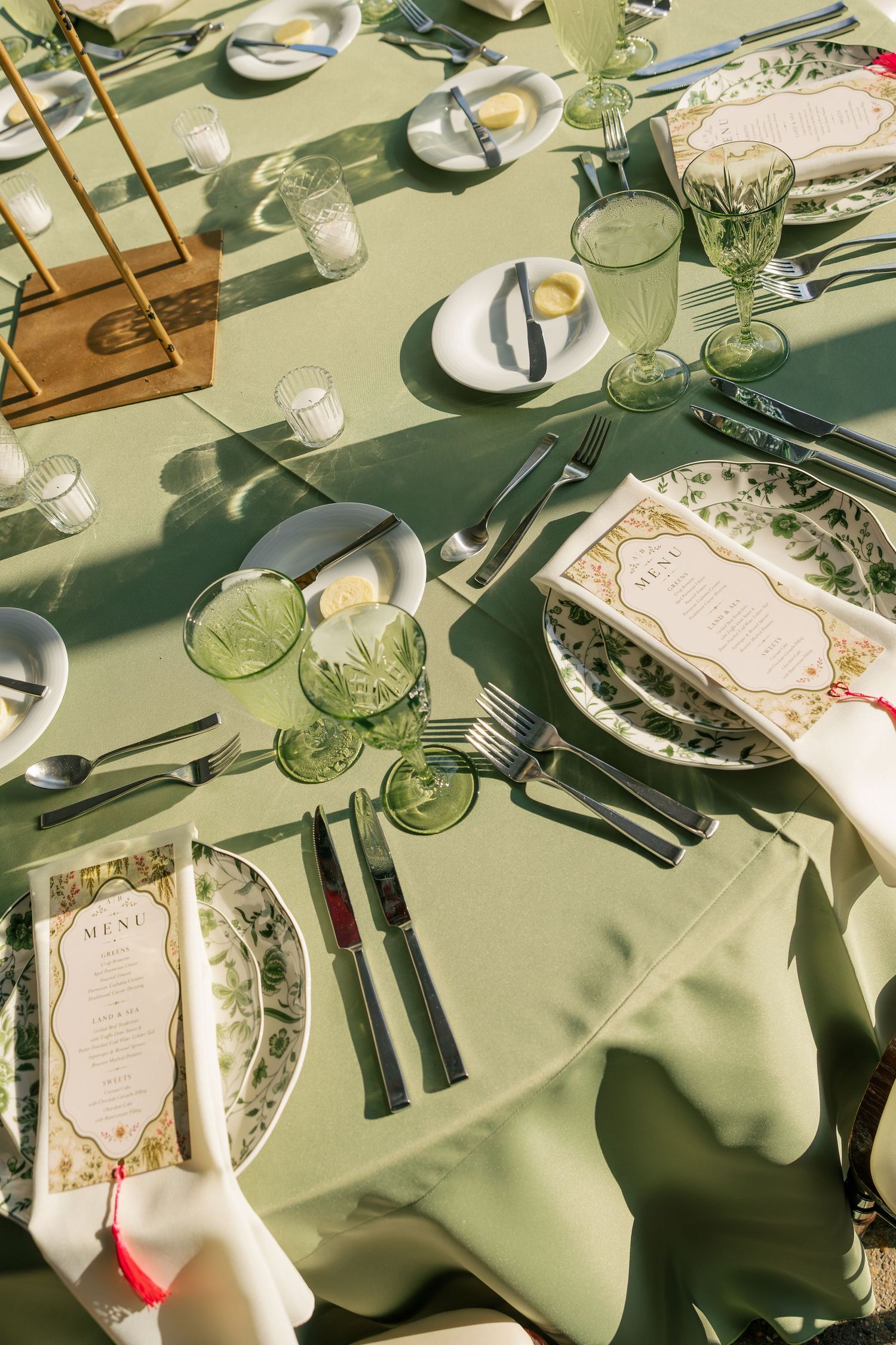 Elegant wedding reception tablescape with sage green linens, green glassware, and floral menu cards.