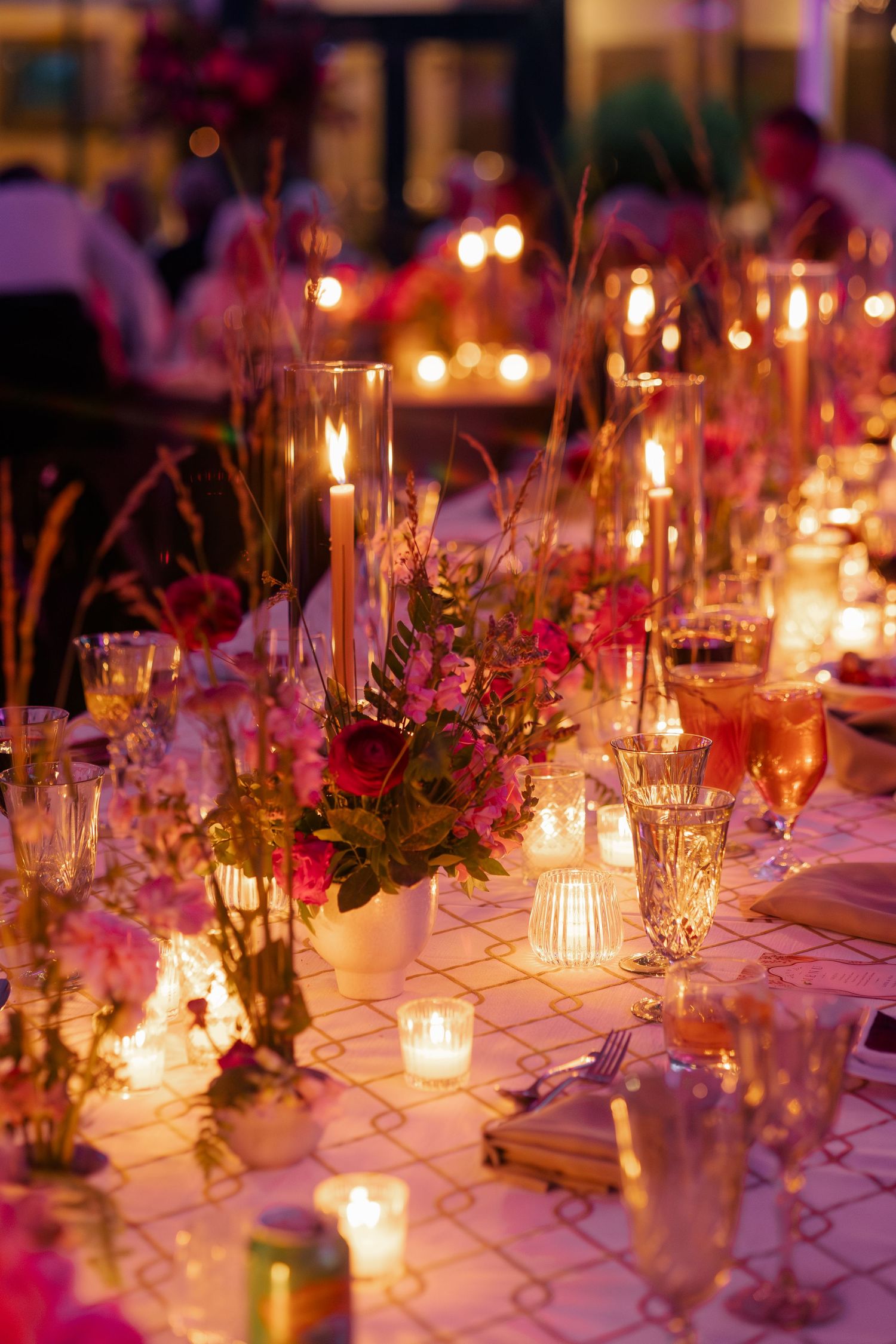 Elegant wedding reception table with pink floral centerpieces, crystal glassware, and romantic candlelight.