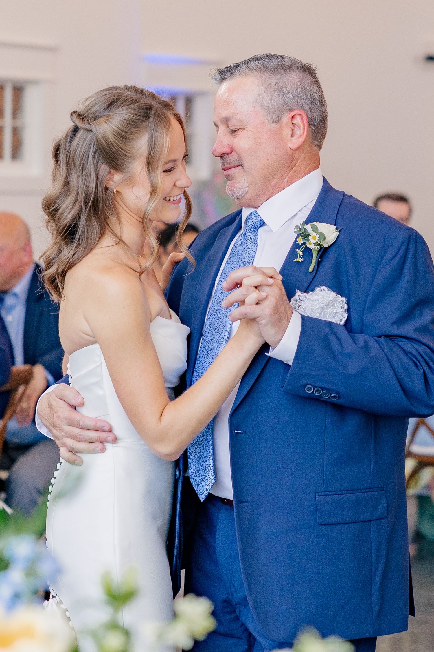 Bride in white strapless gown shares emotional father-daughter dance at wedding reception.