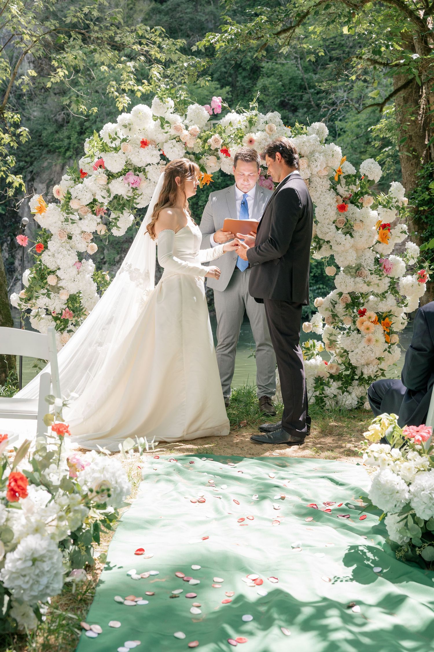 Bride and groom exchange vows under a stunning circular white floral arch at an outdoor wedding ceremony.